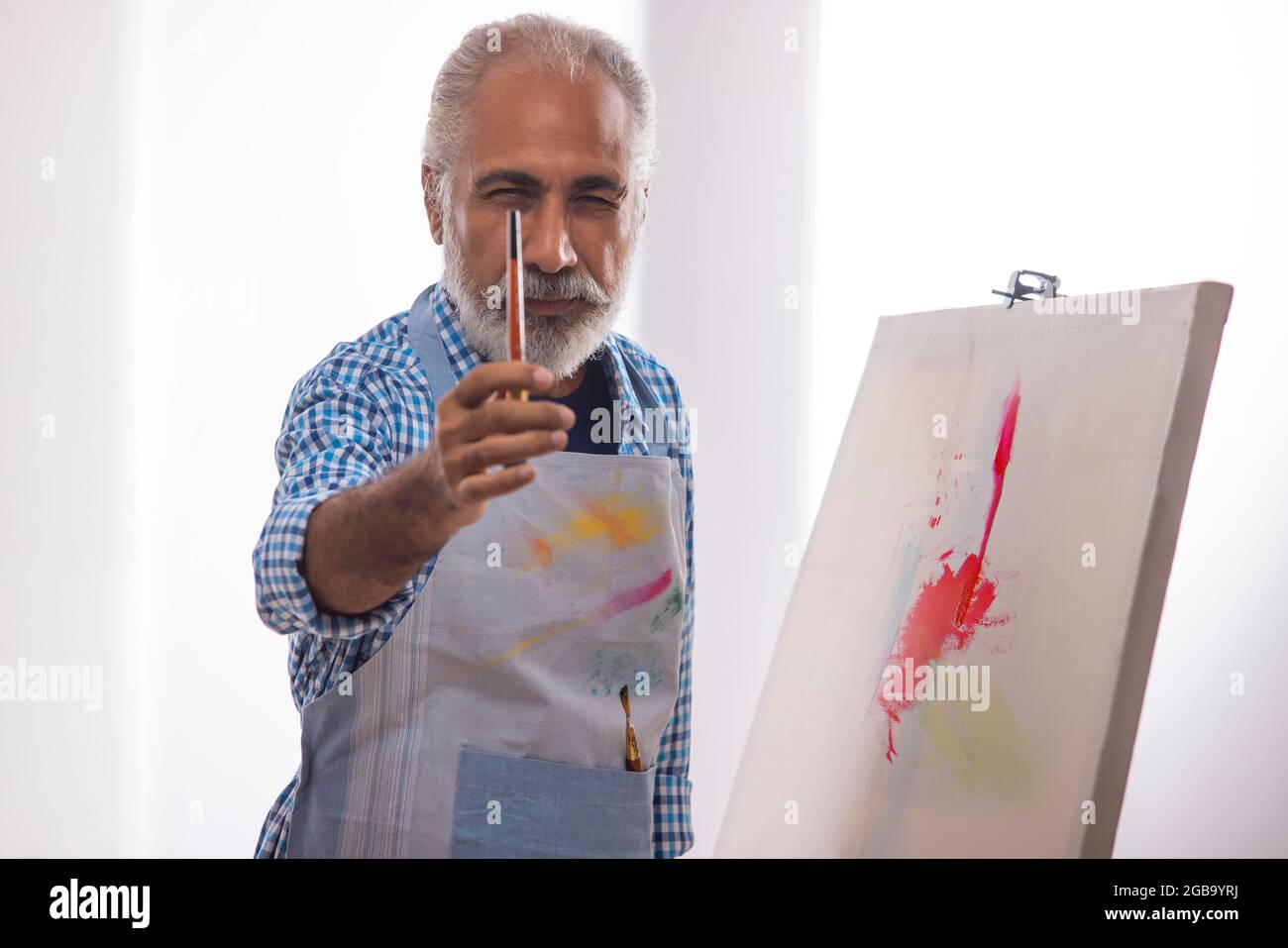 AN OLD MAN POSING IN FRONT OF CAMERA WITH PAINTBRUSH IN HAND Stock