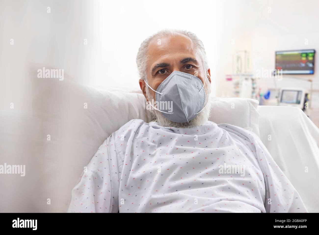 AN OLD MAN WEARING FACE MASK LOOKING AT CAMERA WHILE RESTING Stock Photo