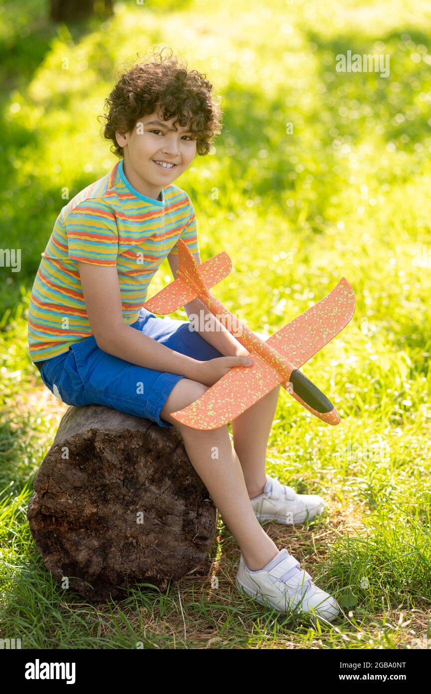 Boy with toy plane sitting on tree stump Stock Photo