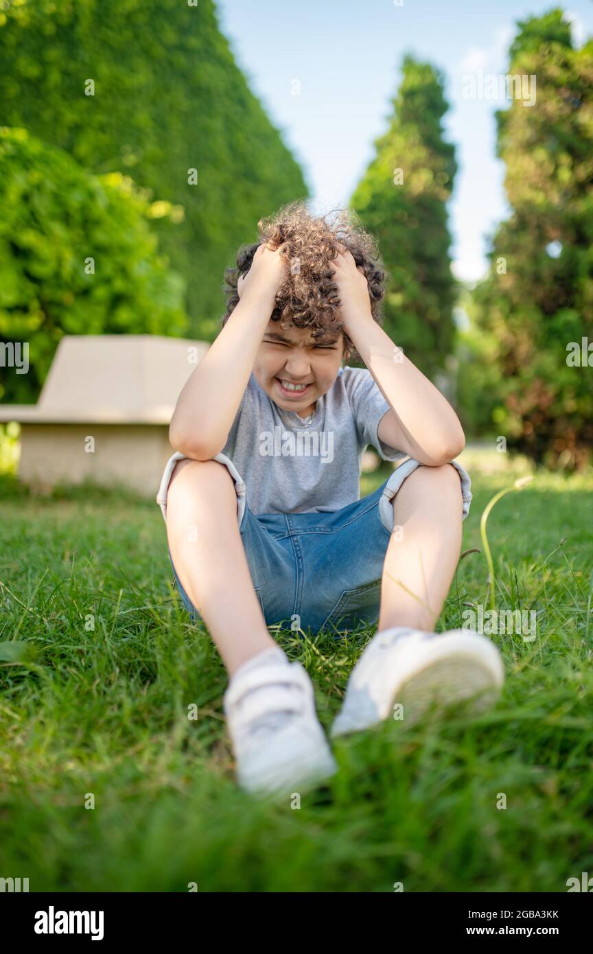 Boy holding his head sitting on the grass Stock Photo