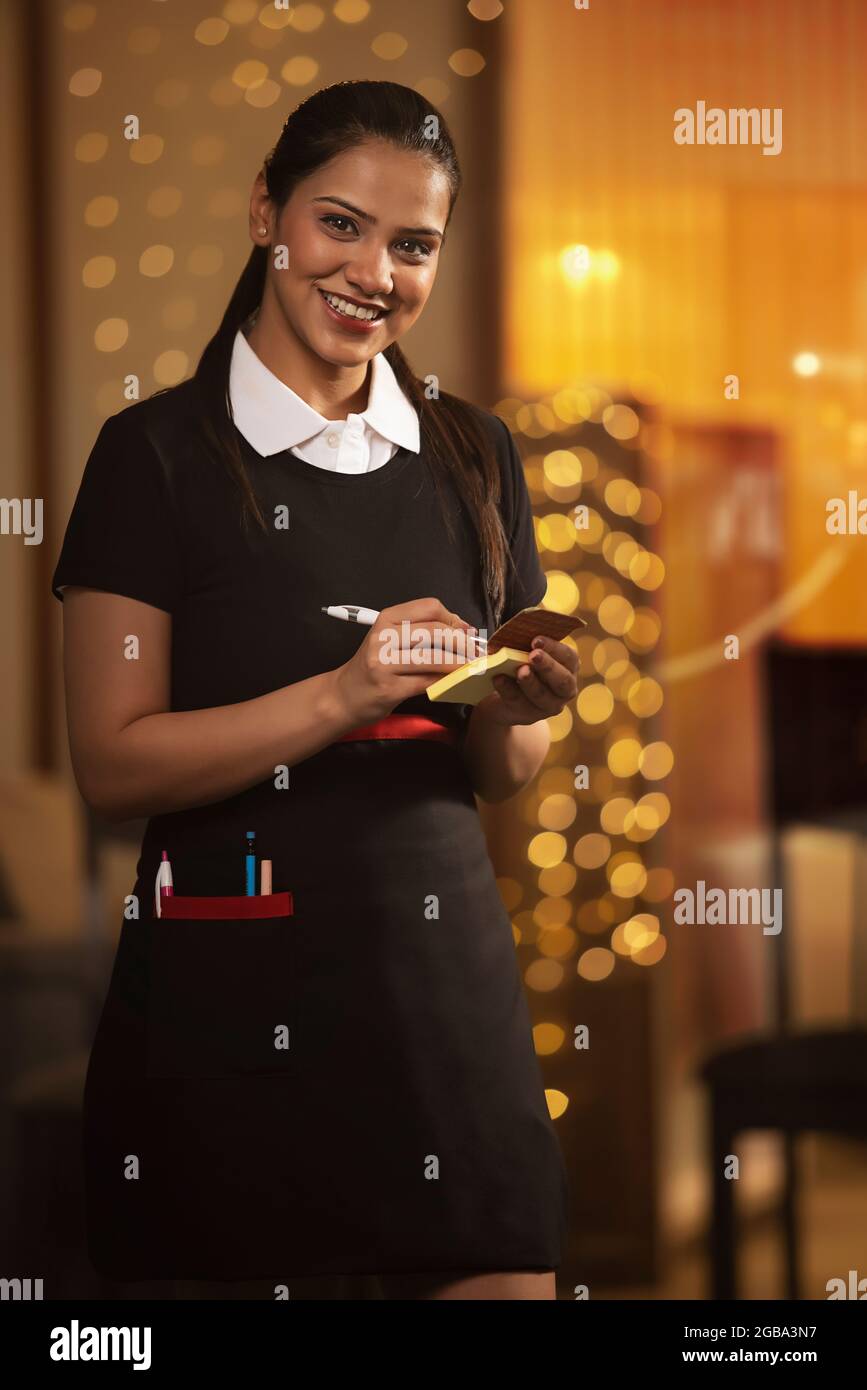 A HAPPY WAITRESS LOOKING AT CAMERA WHILE TAKING DOWN ORDERS Stock Photo