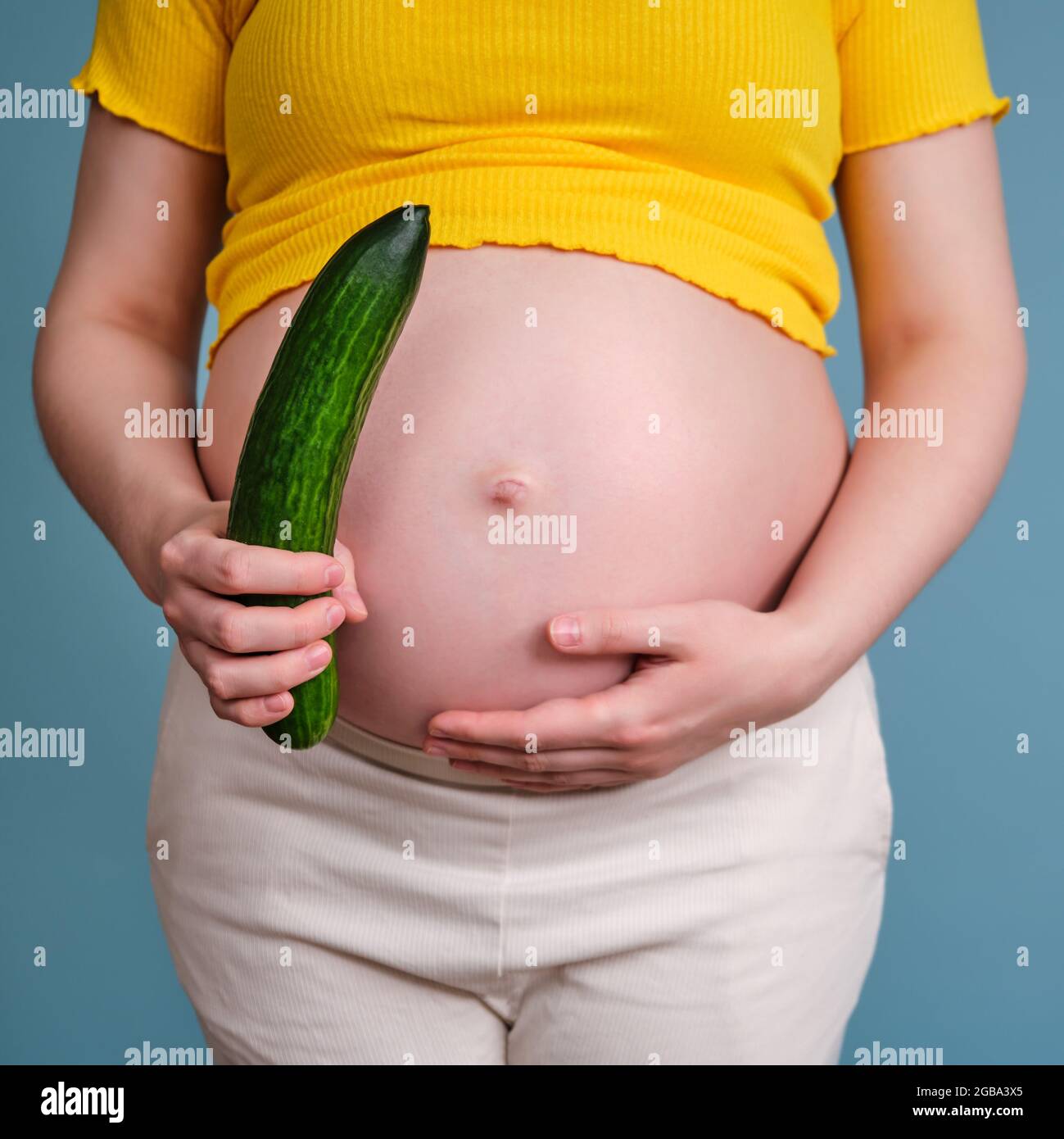 A pregnant woman holds a large green cucumber in her hand Stock Photo