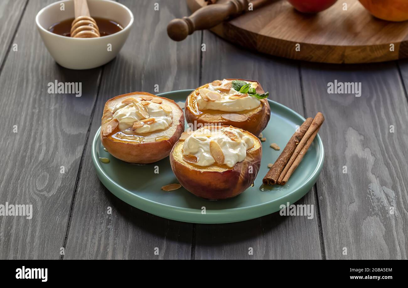 Baked peaches on a plate with mint leaf, cinnamon, non-dairy cream cheese, honey, and almond flakes. Stock Photo