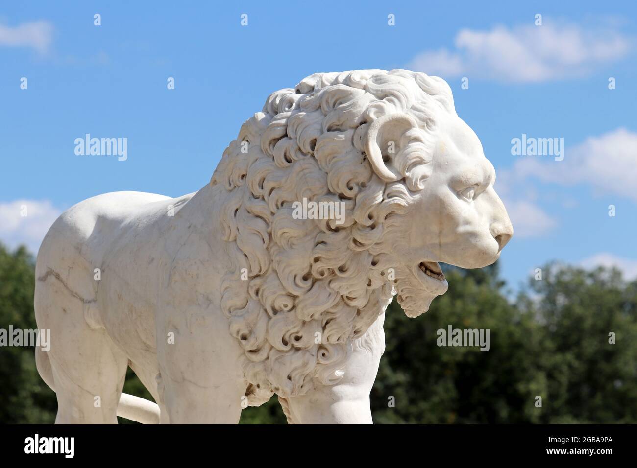 Stone lion decorating summer park. Marble sculpture on blue sky and green trees background Stock Photo