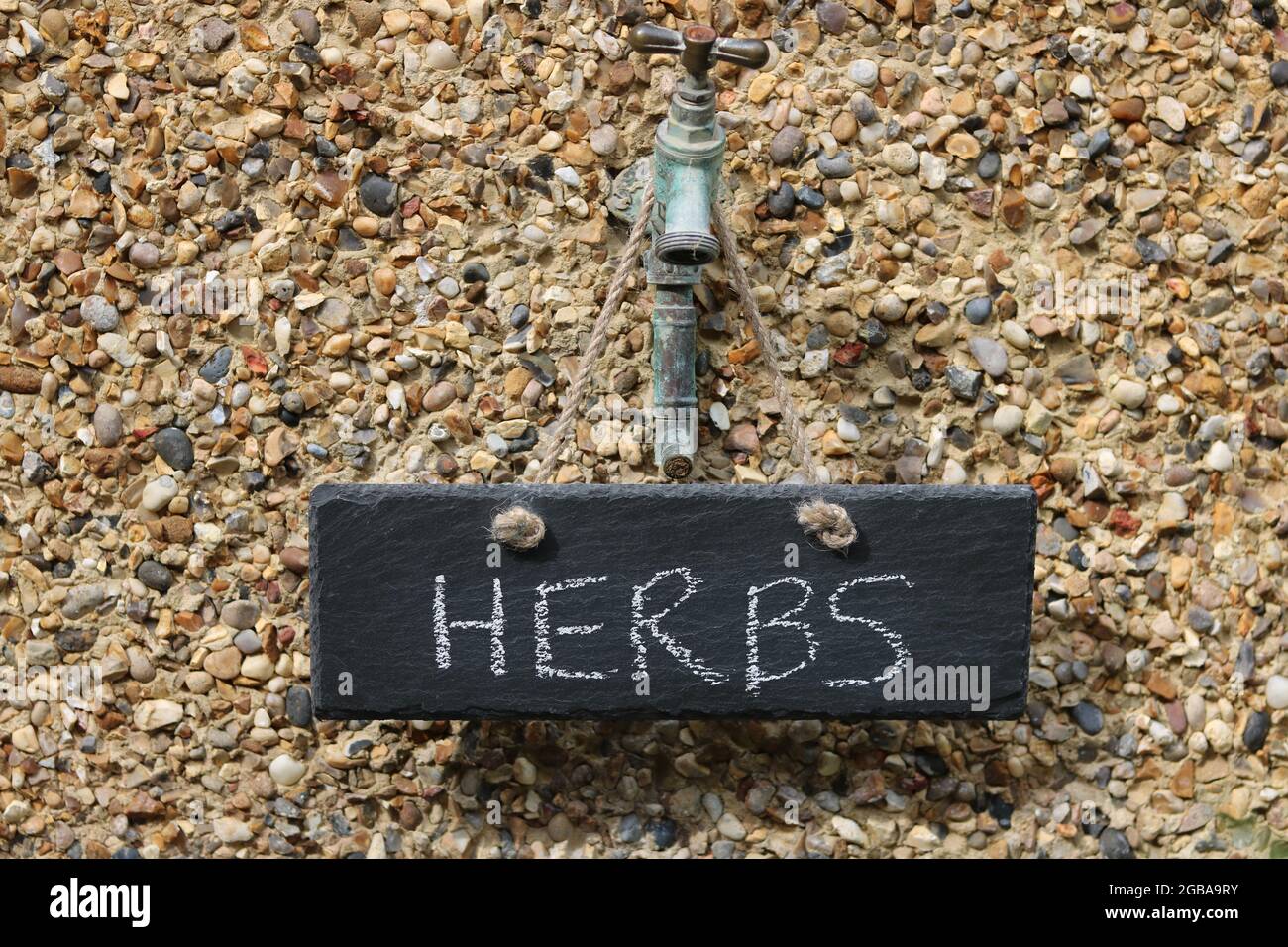 Dark grey slate sign saying Herbs hanging off outdoor tap Stock Photo