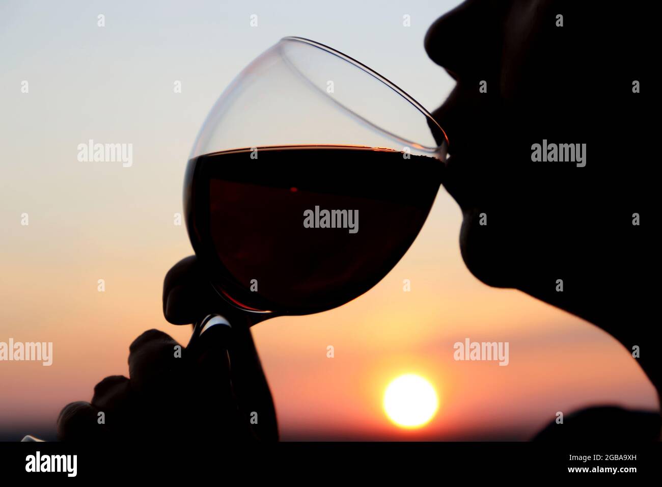 Woman drinking red wine, silhouette of face with glass at sunset. Enjoying alcohol, romantic dinner at the resort, luxury life Stock Photo