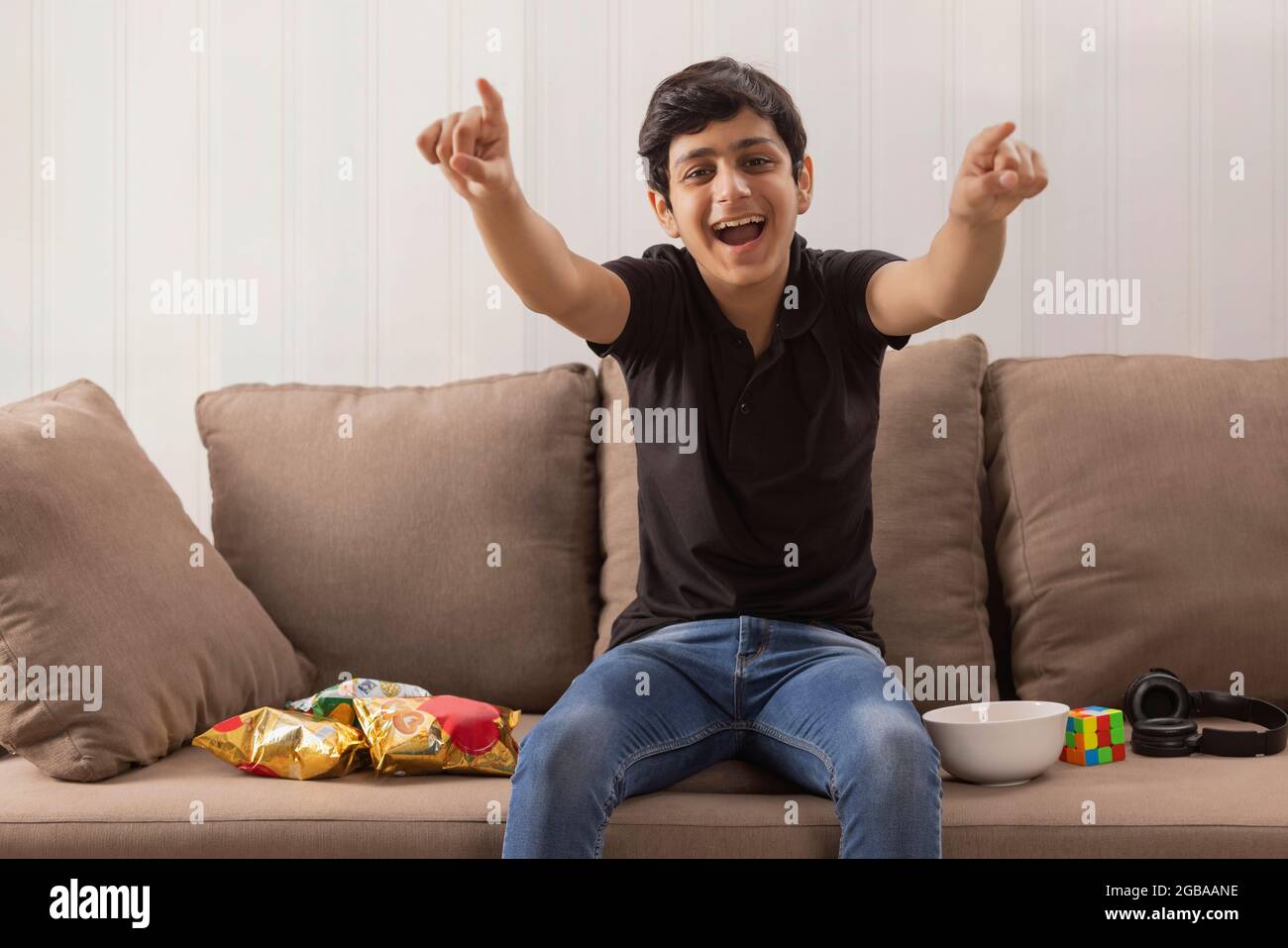 A HAPPY TEENAGE BOY CHEERING WHILE ENJOYING AT HOME Stock Photo
