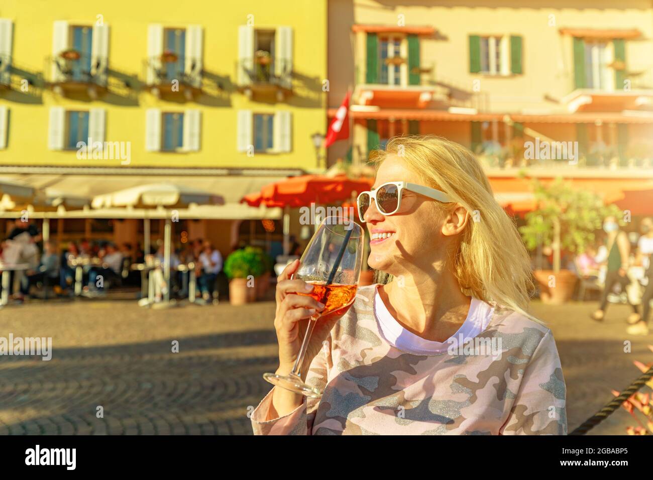 Woman tourist drinking a cocktail by the lakefront corniche in an open pub of Ascona historic city in Switzerland, in Ticino Canton on Lake Langensee. Stock Photo