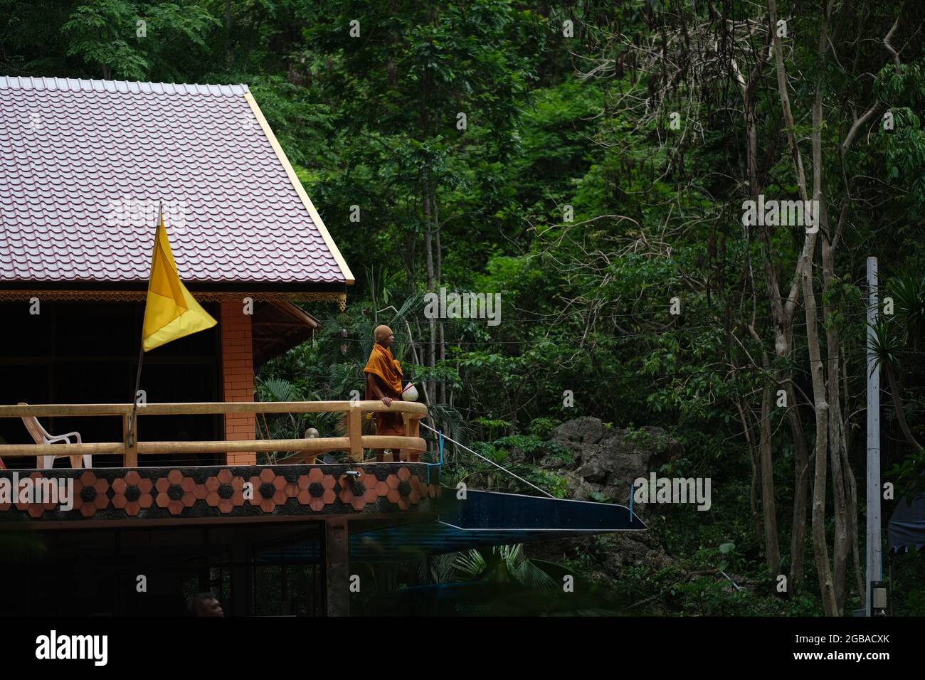 A Buddhist monk observes a forest from upper floor of his residence