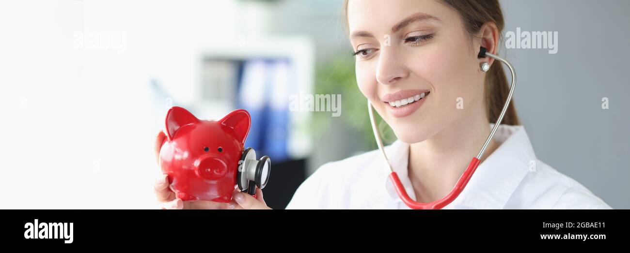 Smiling female doctor stethoscope listens to piggy bank piggy bank