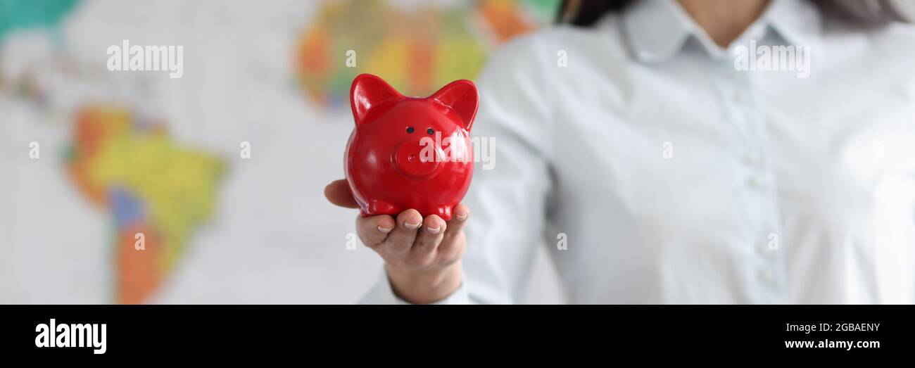 Young smiling woman holding red pig piggy bank on background of world map Stock Photo