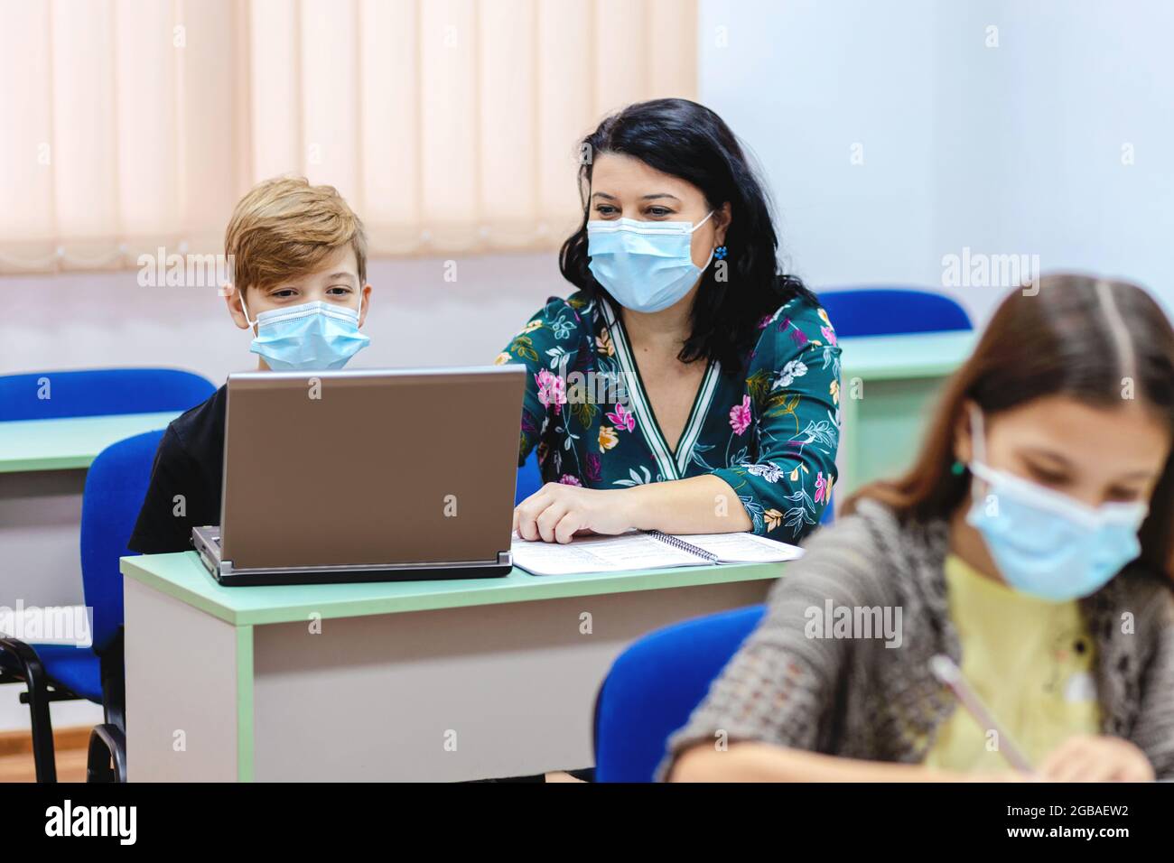 Children and teacher with face mask back to school in classroom after covid-19 lockdown Stock Photo