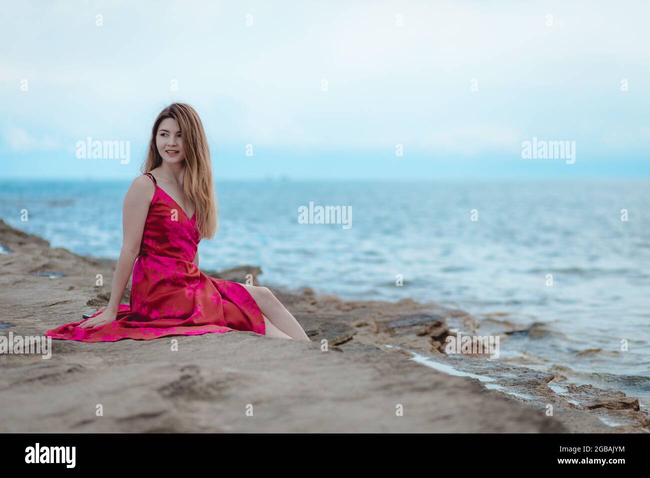Young woman in a pink dress sitting on the beach Stock Photo - Alamy