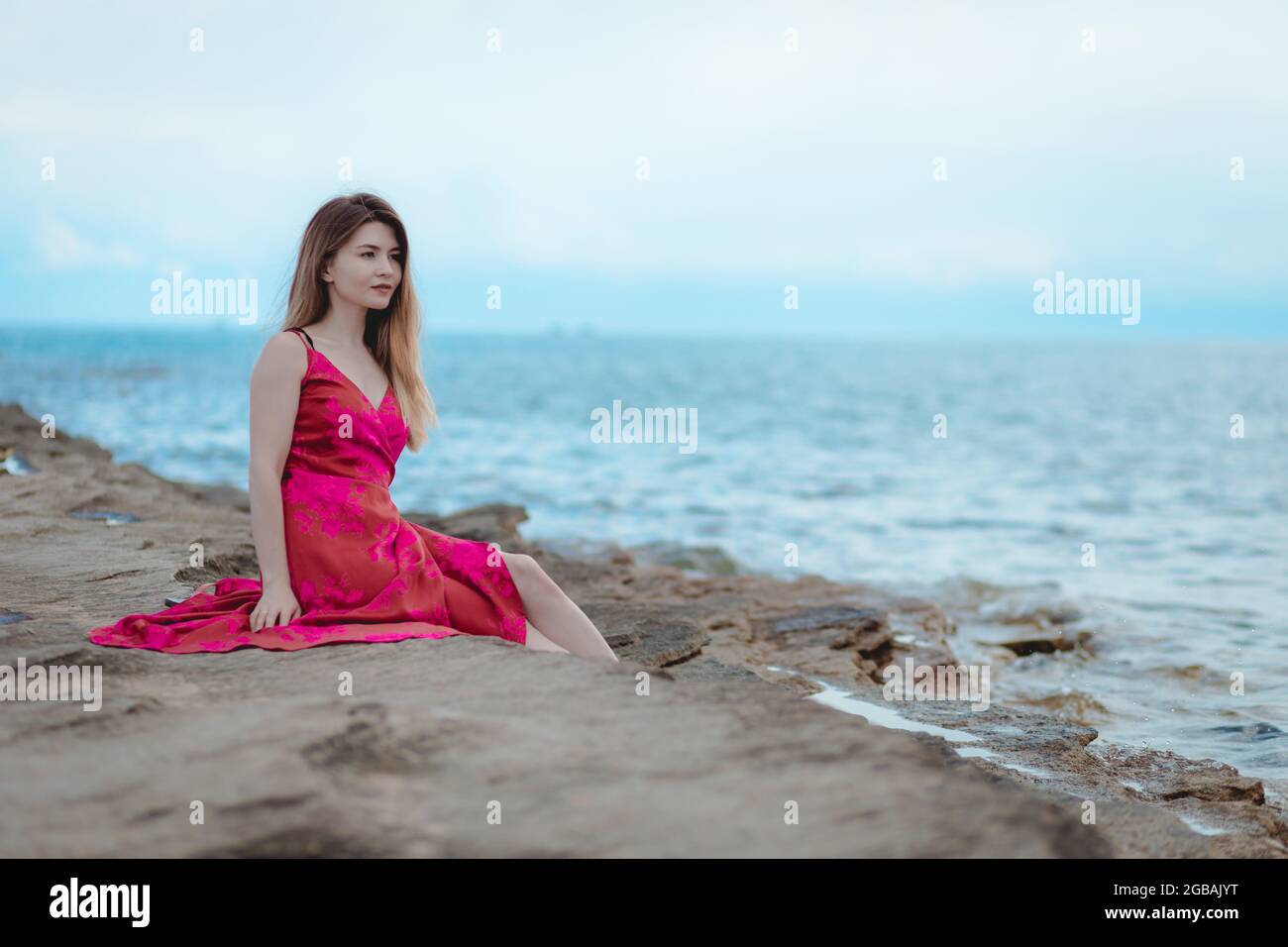 Young woman in a pink dress sitting on the beach Stock Photo - Alamy