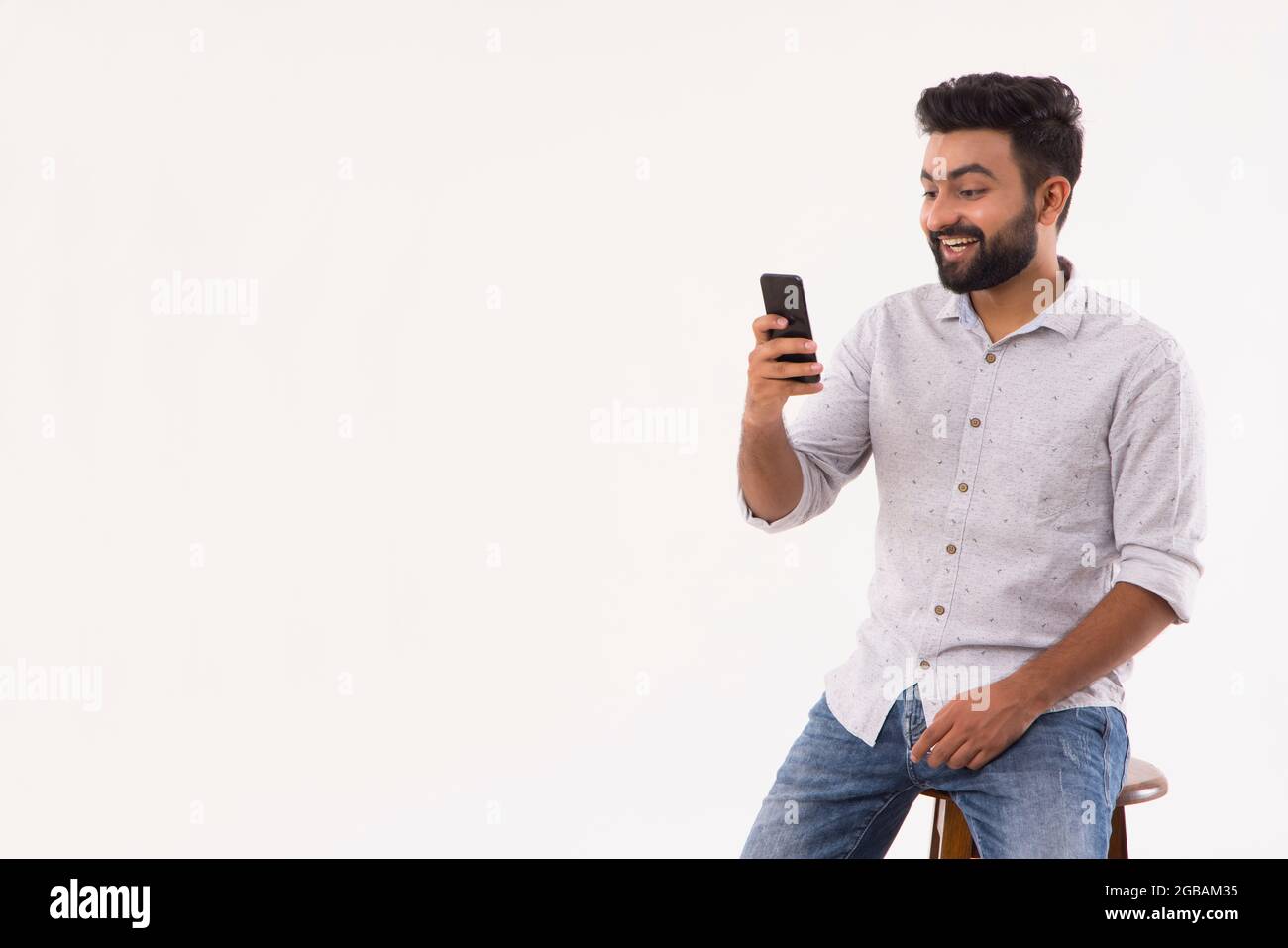 A BEARDED YOUNG MAN LOOKING SURPRISED WHILE USING MOBILE Stock Photo