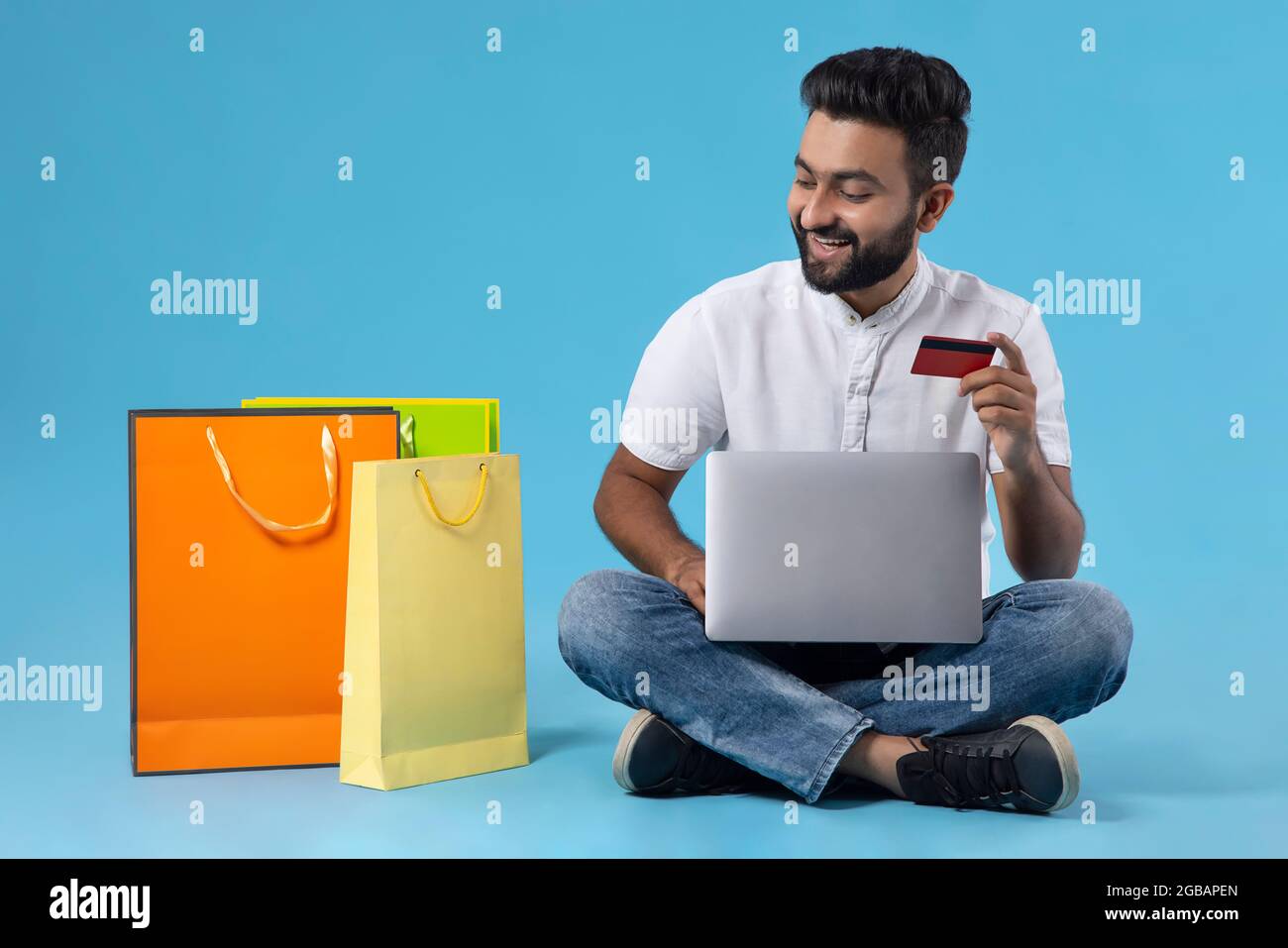 A YOUNG BEARDED MAN LOOKING AT SHOPPING BAGS WHILE HOLDING DEBIT CARD Stock Photo