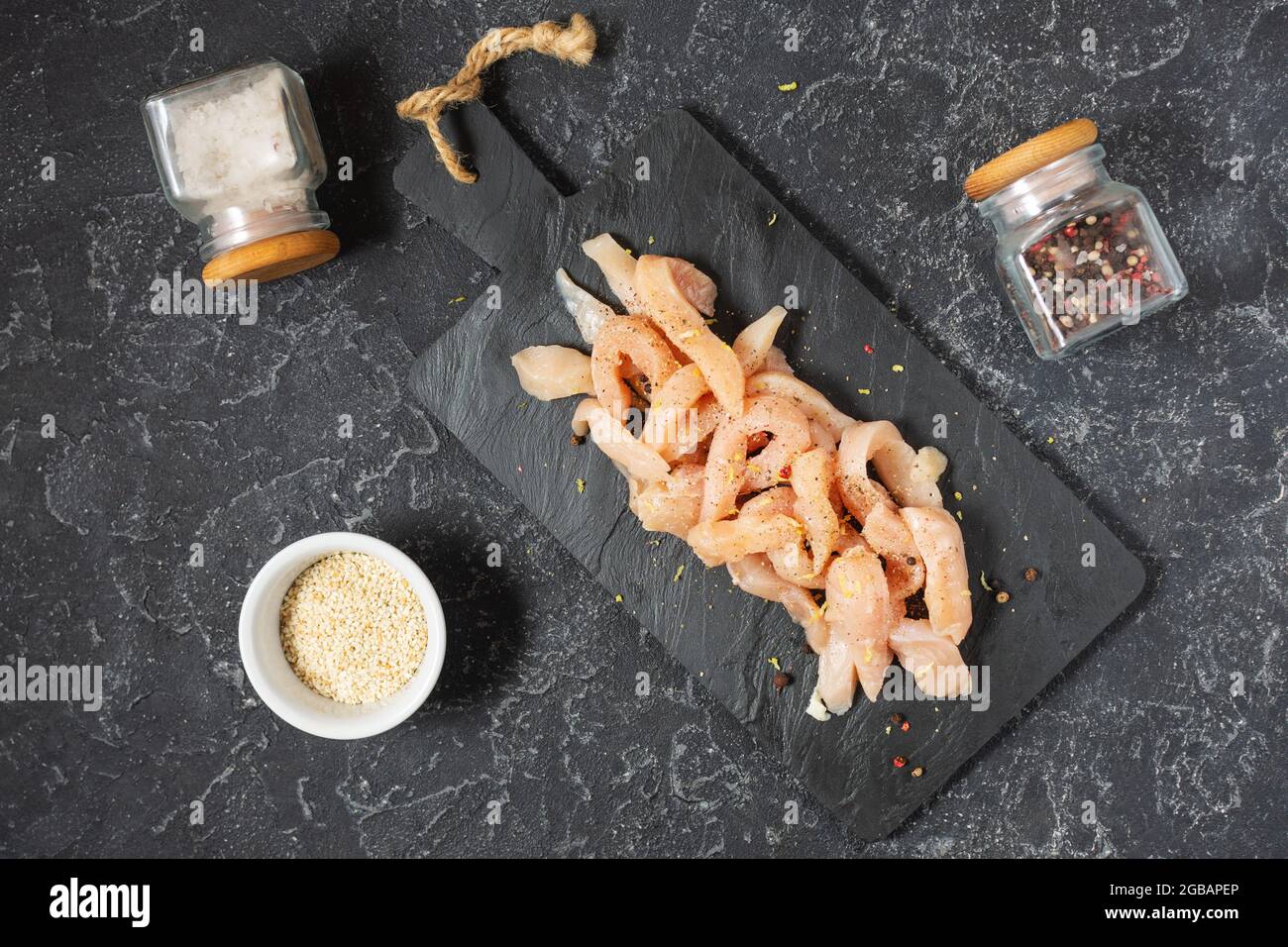 fresh raw chicken breast cut in strips for a goulash or stir fry seasoned with spice rub heaped on a black stone background. Top view Stock Photo