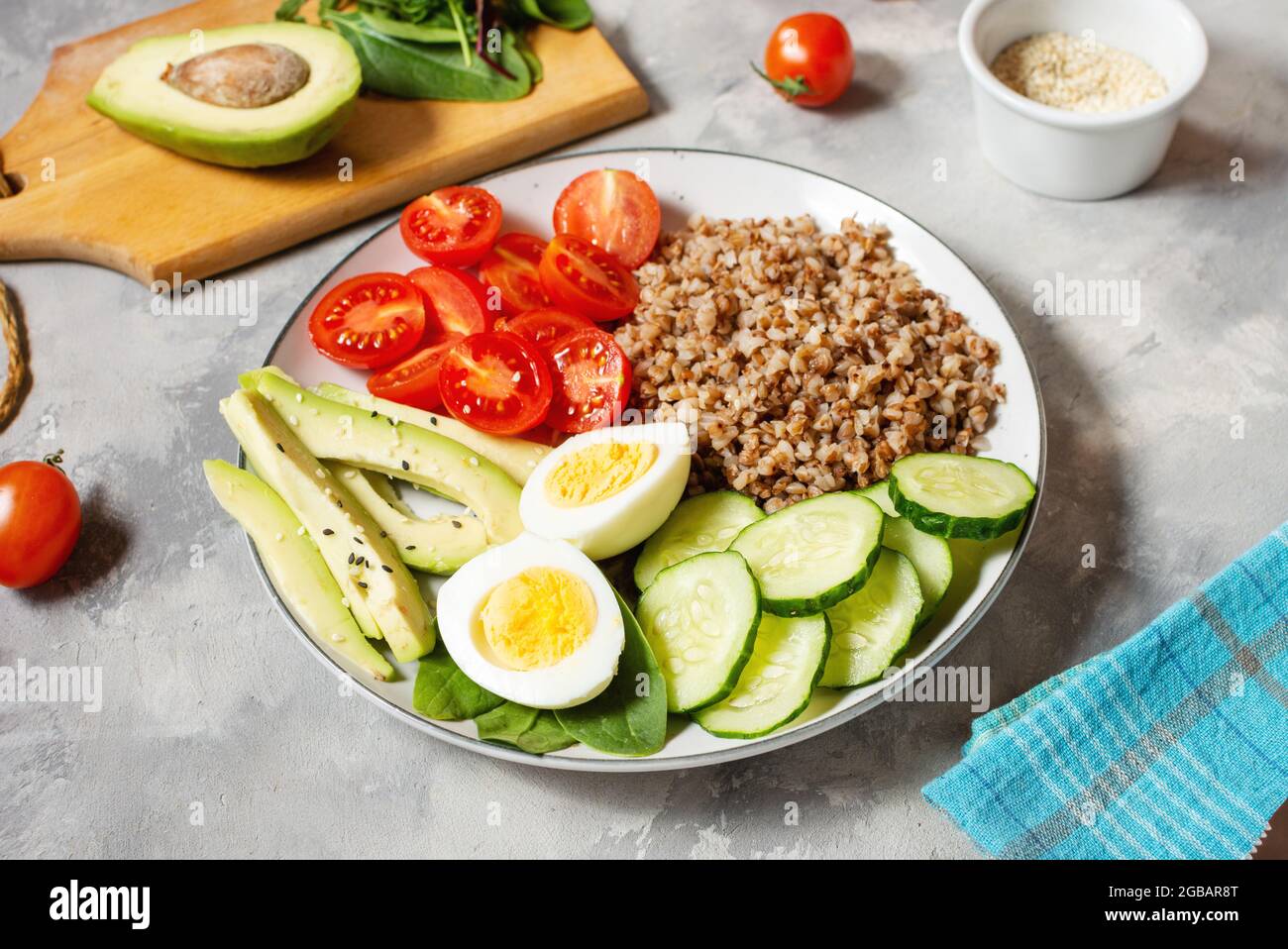Vegan lunch bowl with avocado, egg, cucumber, tomato and buckwheat on a concrete background Stock Photo