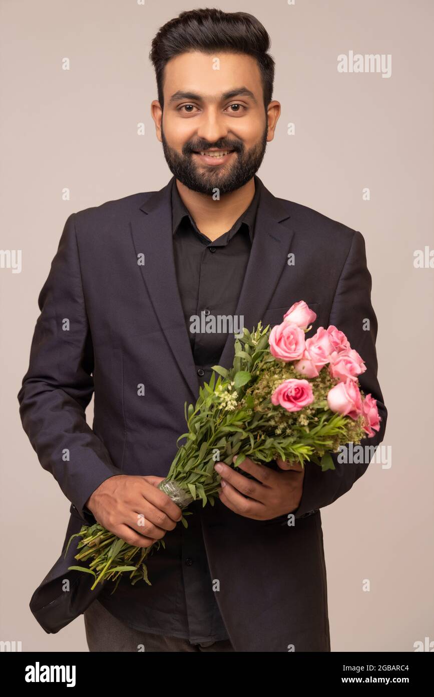 A WELL-GROOMED YOUNG MAN STANDING WITH BOUQUET IN HAND Stock Photo