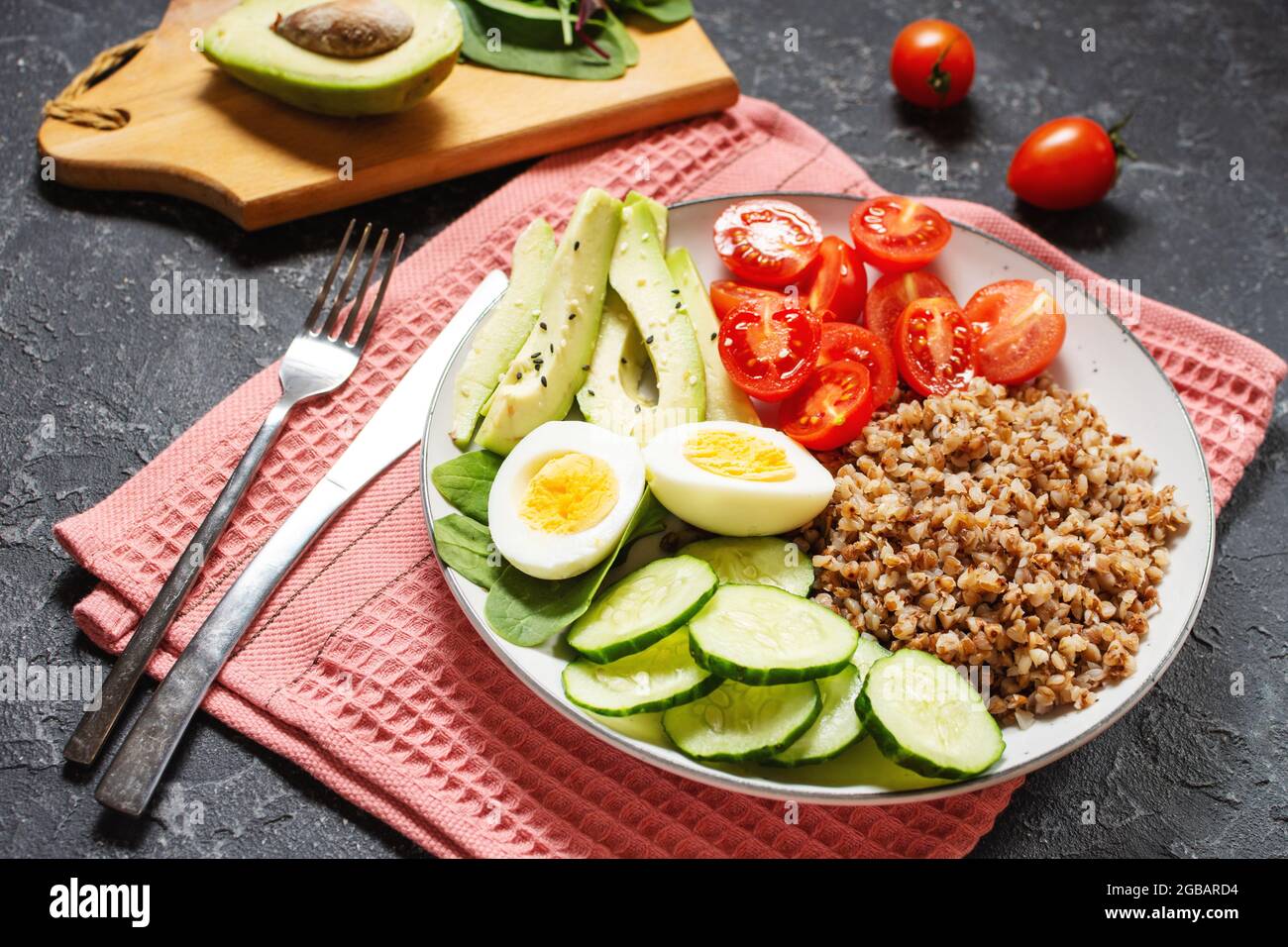 Vegan lunch bowl with avocado, egg, cucumber, tomato and buckwheat on black stone background Stock Photo