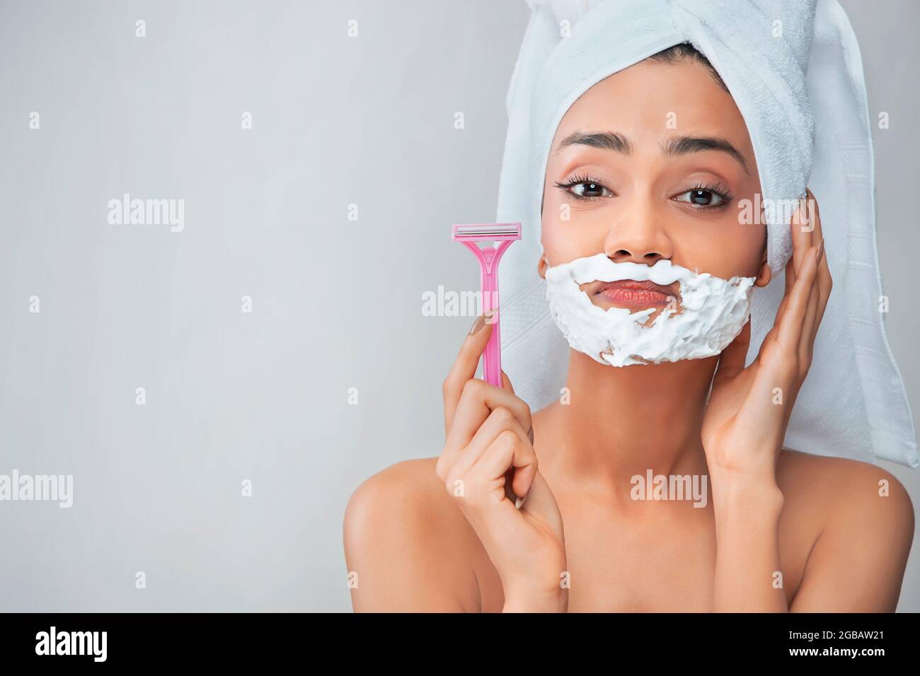 A young woman with hair removal cream on her face and razor in her hand. Stock Photo