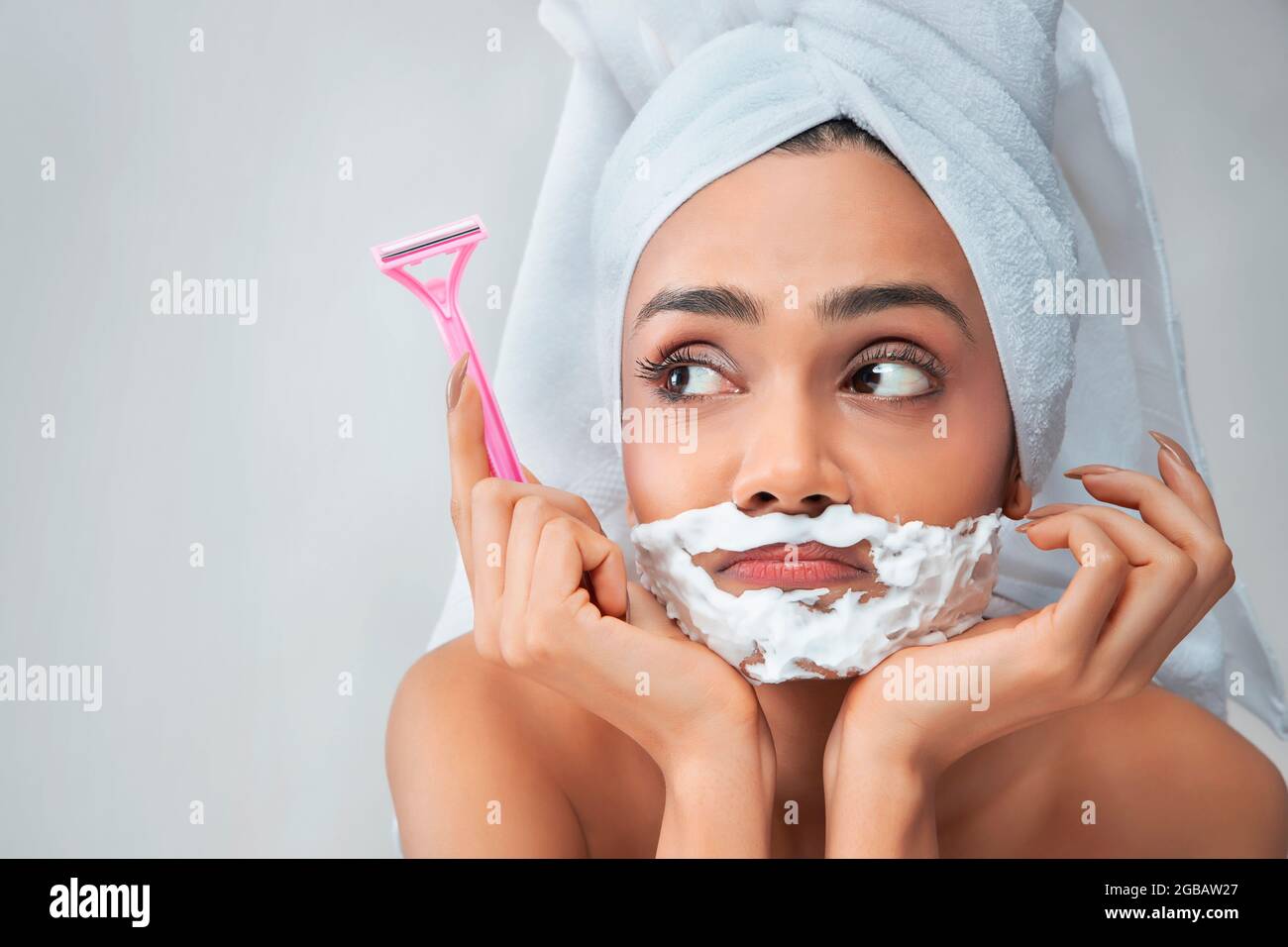 A young woman with hair removal cream on her face and razor in her hand. Stock Photo