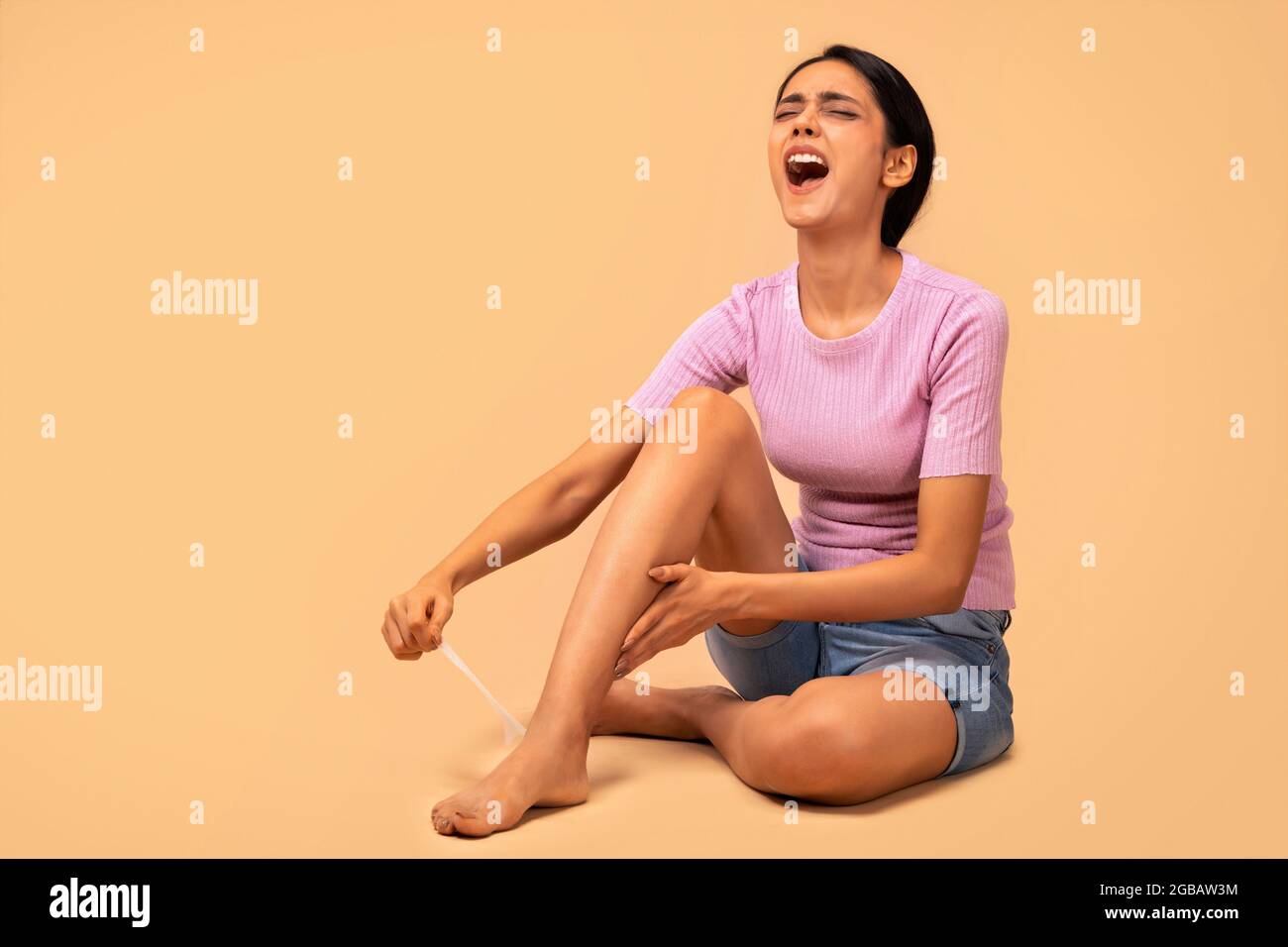 A young woman using wax strips on her legs to remove body hair Stock