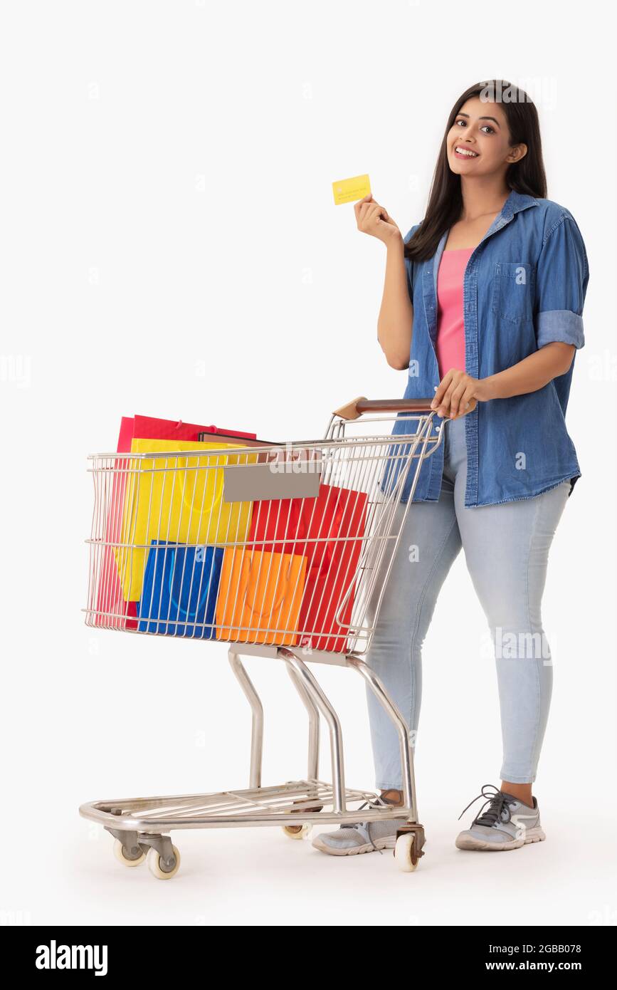 A young woman with credit card in hand moving a trolley containing colorful shopping bags. Stock Photo