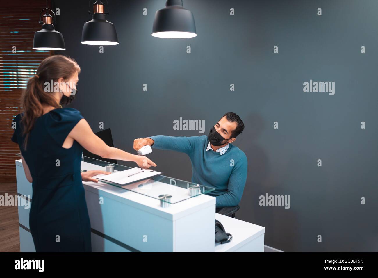 Two diverse businesspeople wearing face masks and taking temperature at reception Stock Photo