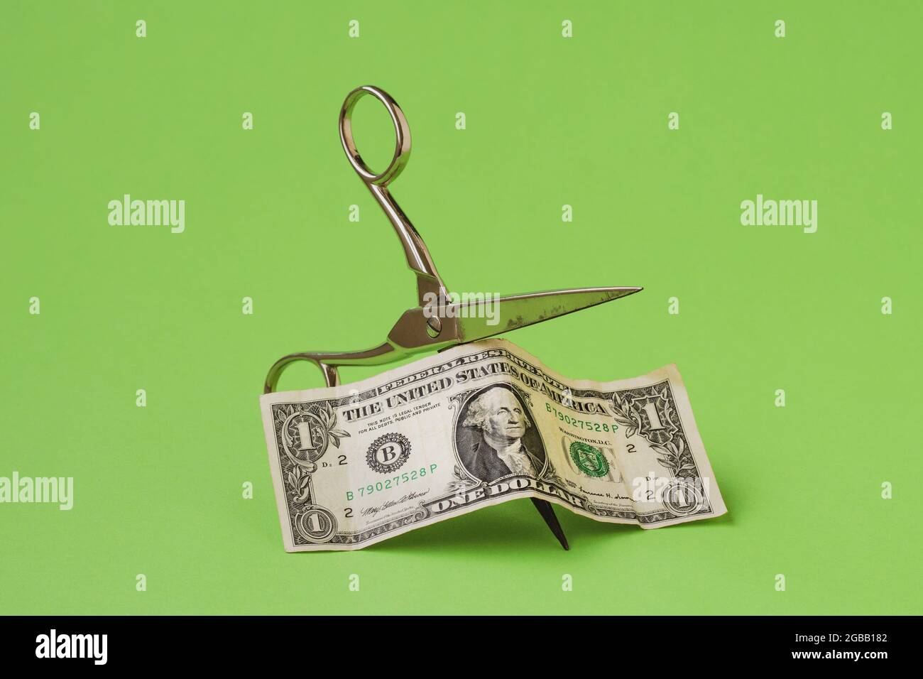 Cutting one dollar with scissors on green background. Devaluation of money. Stock Photo