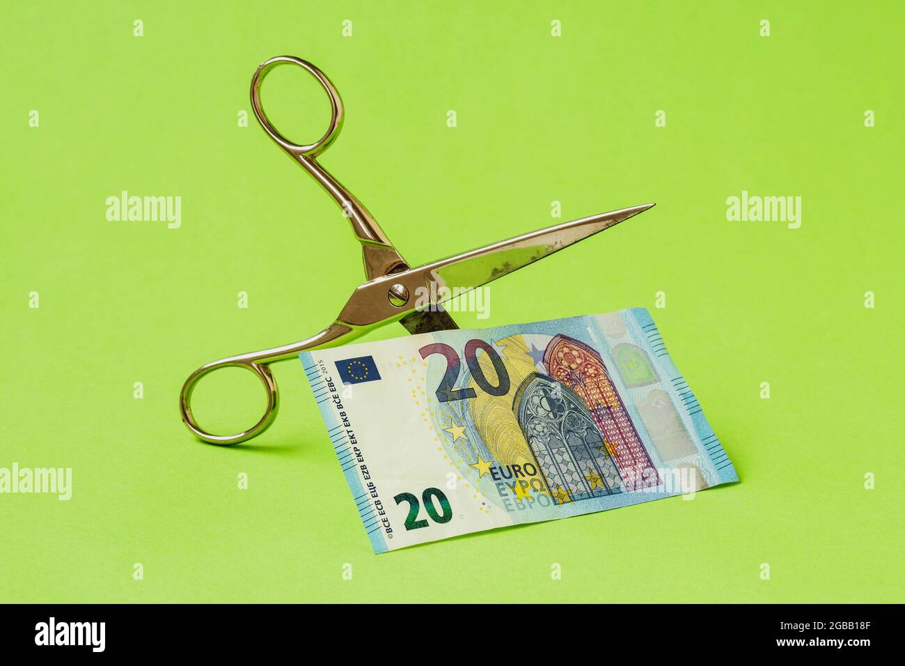 Cutting twenty Euro note with scissors on green background. Devaluation of Euro currency. Stock Photo