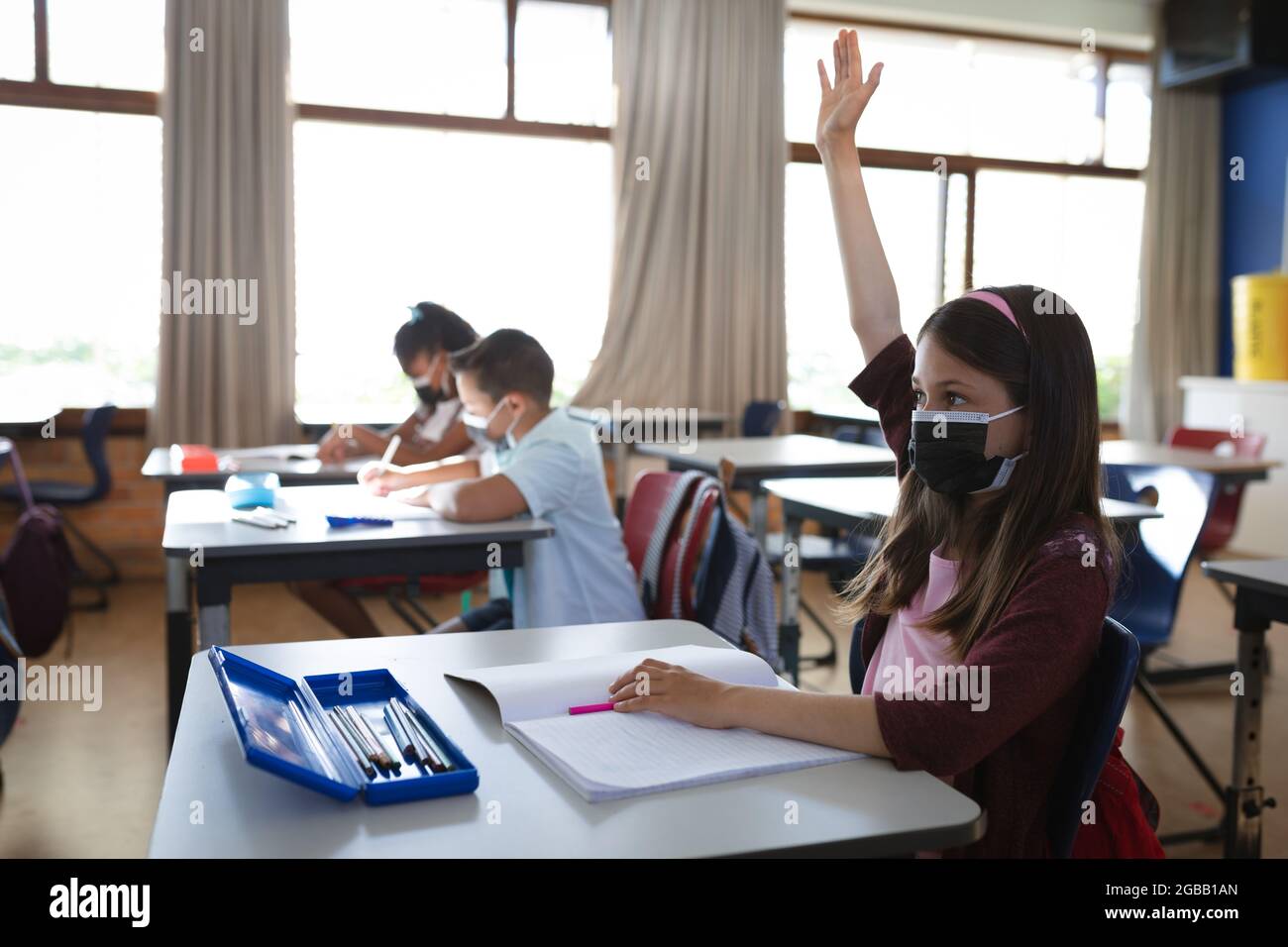 Caucasian girl wearing face mask raising her hand while sitting on her ...
