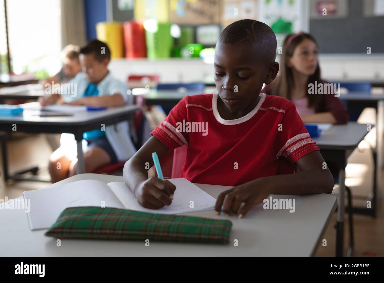 African american boy studying while sitting on his desk in the class at ...