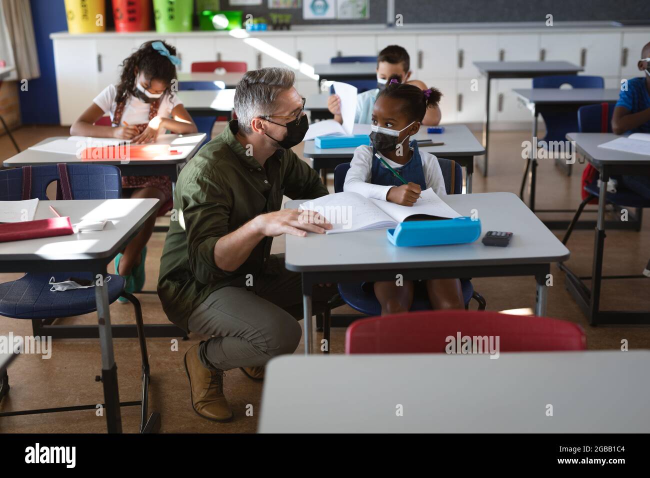 Caucasian male teacher wearing face mask teaching african american girl