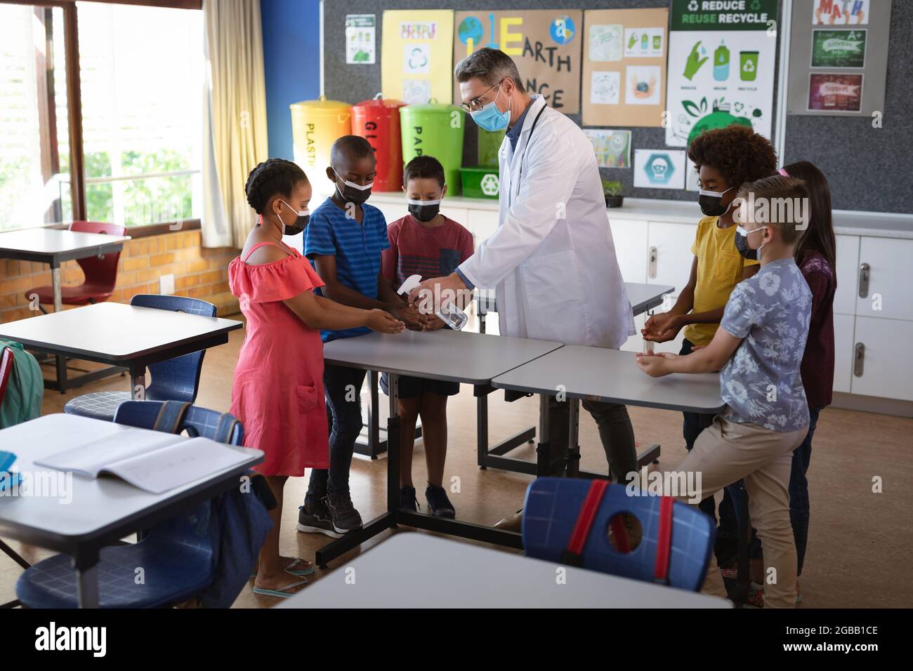 Caucasian male doctor wearing face mask spraying hand sanitizer on