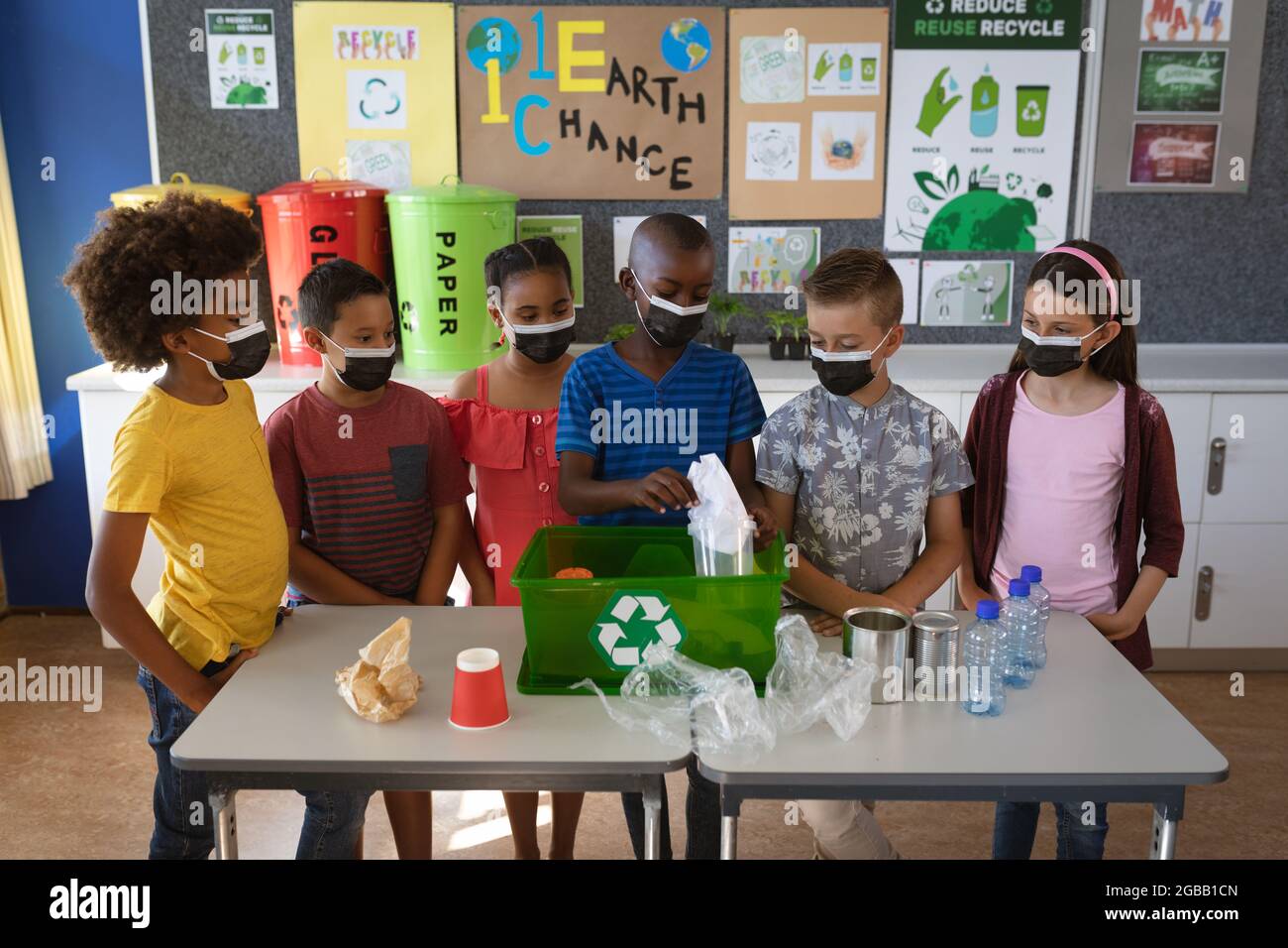 Group of diverse students wearing face masks putting recyclable plastic items in tray at school Stock Photo