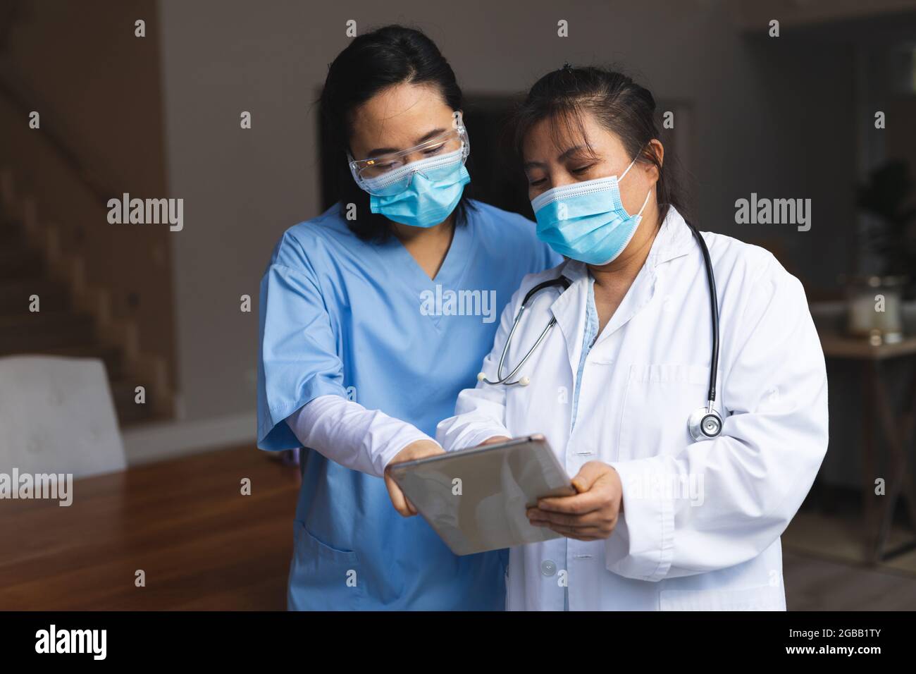 Two asian female doctors wearing face masks at home using tablet Stock Photo