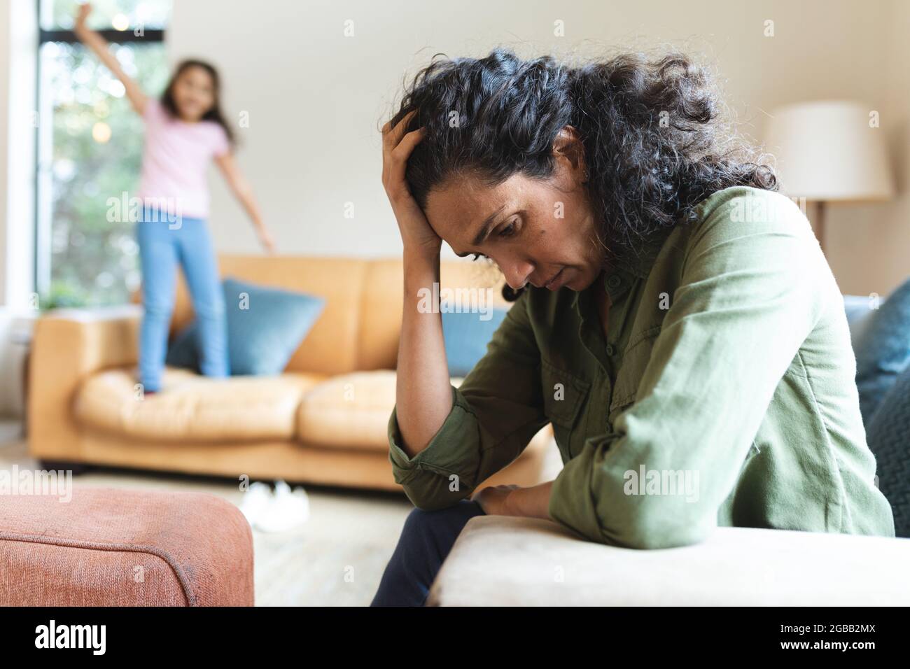 Tired mixed race mother sitting on sofa, having headache Stock Photo