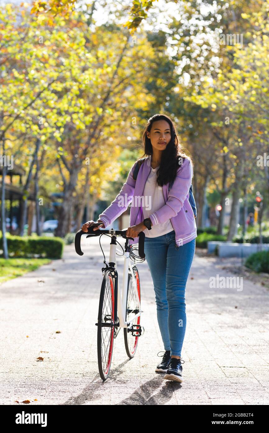 Smiling asian woman wheeling bike in sunny park Stock Photo