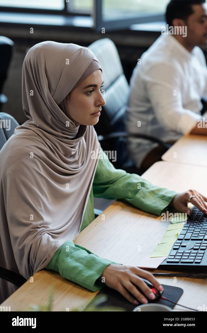 Pretty Muslim businesswoman in hijab sitting in front of computer ...