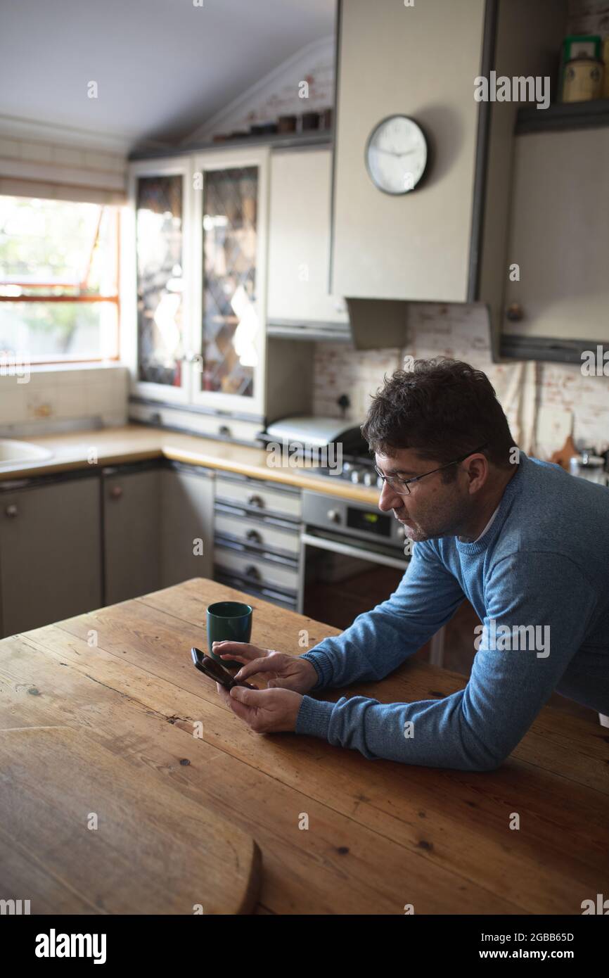 Caucasian man in kitchen standing at table and using smartphone Stock Photo