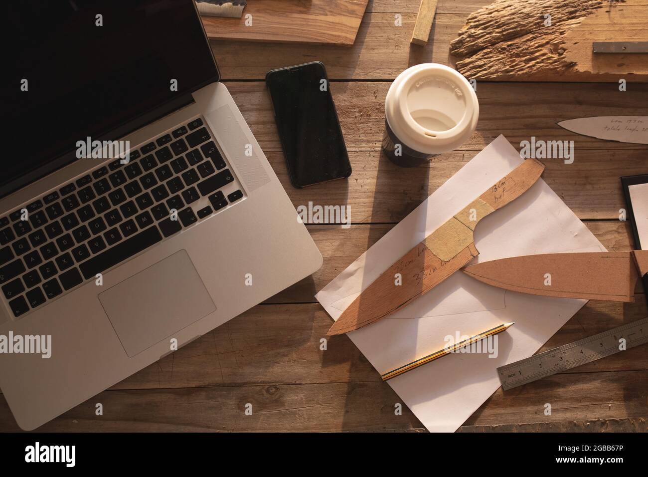 Laptop, smartphone, knife molds and other utensils lying on desk at knife maker workshop Stock Photo