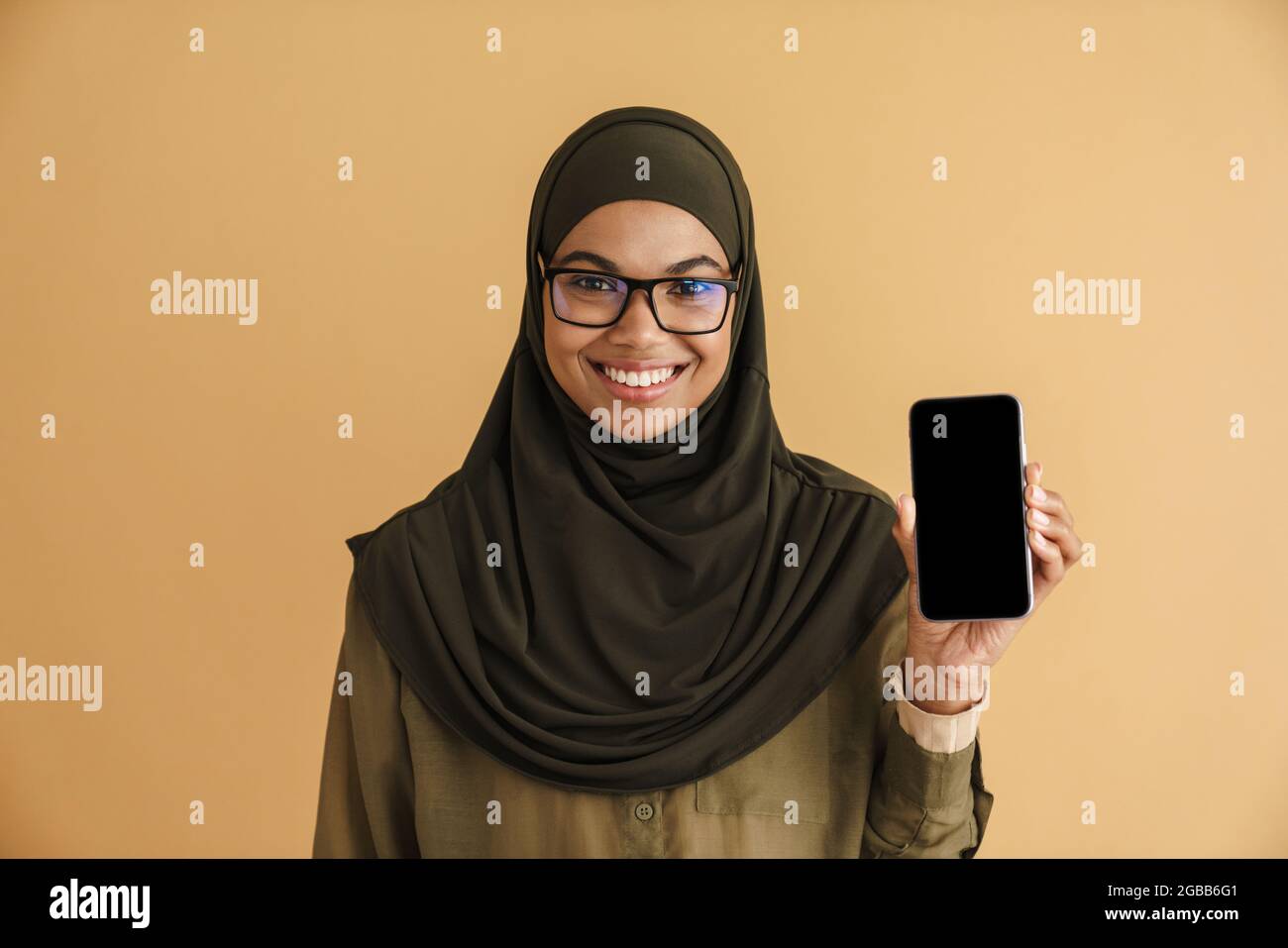 Black muslim woman in hijab smiling and showing mobile phone isolated ...