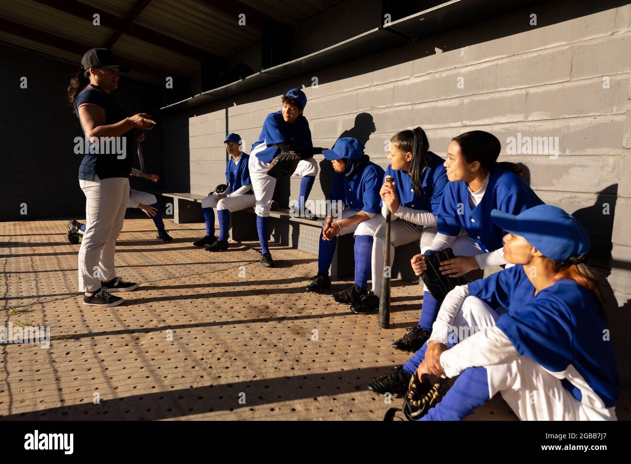 Diverse group of female baseball players sitting on bench, listening to