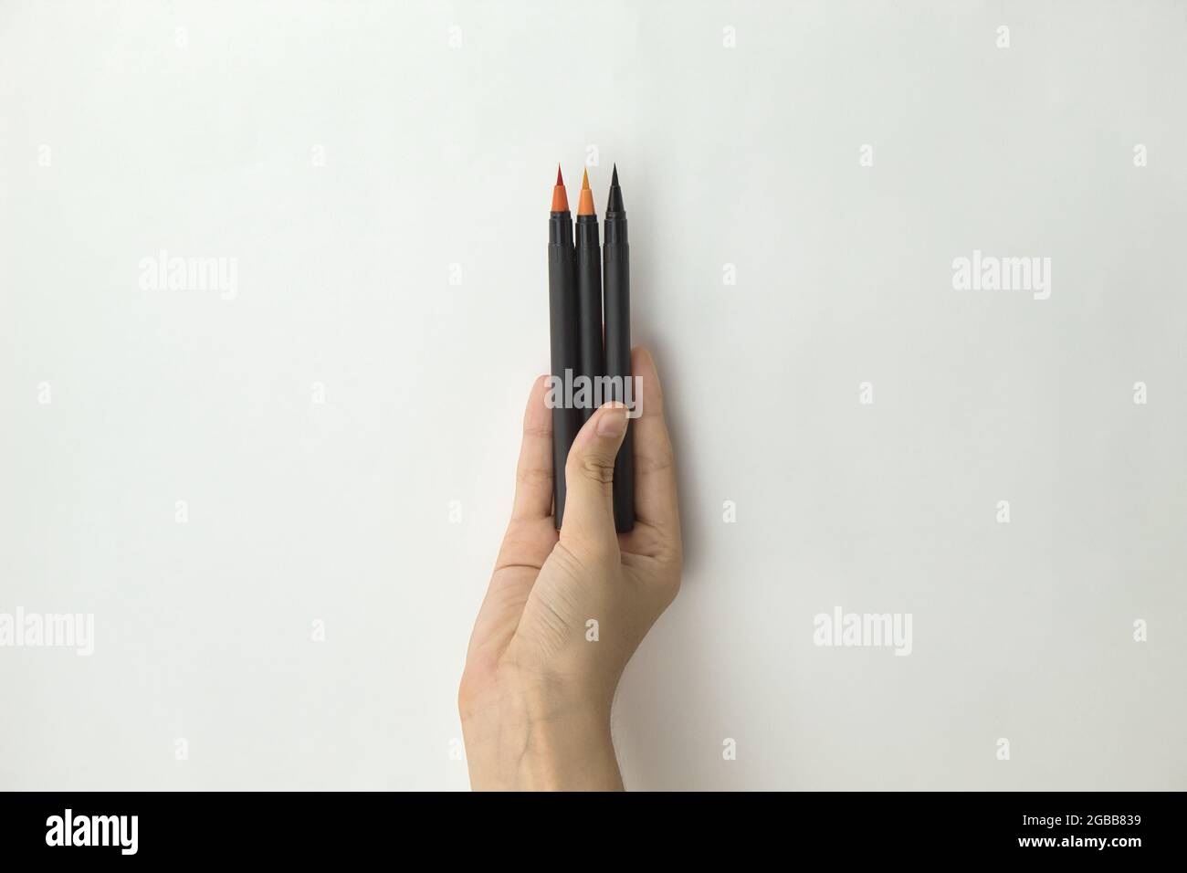 hand of a girl holding a handful of color pens and markers on white