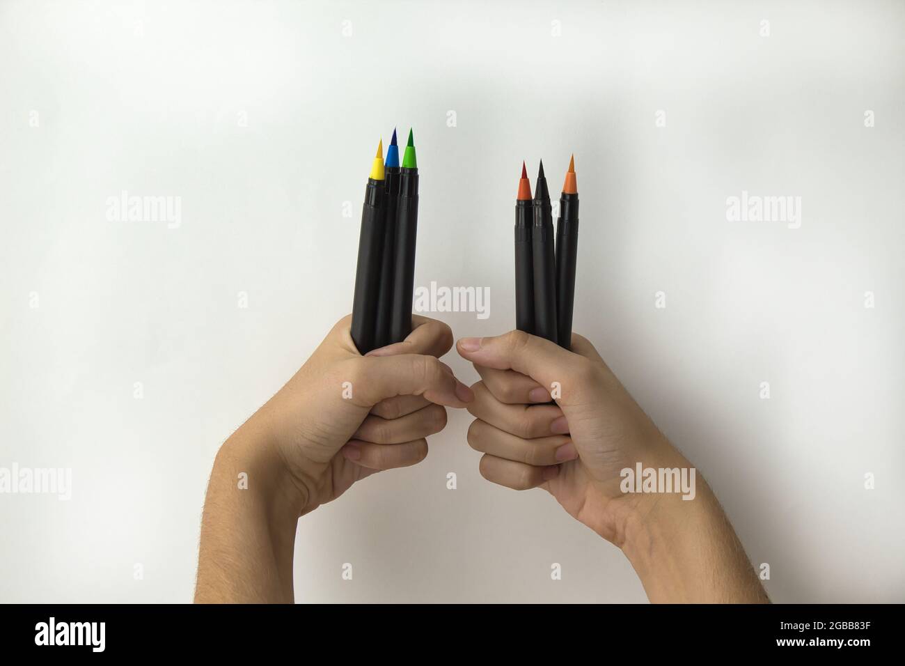 hands of a girl holding a handful of color pens and markers on white