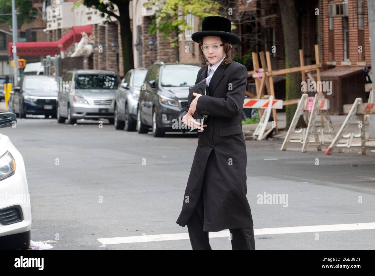 A young orthodox Jewish man who appears to be a teenager, crosses a street in Williamsburg, Brooklyn on the way to morning prayers. Stock Photo