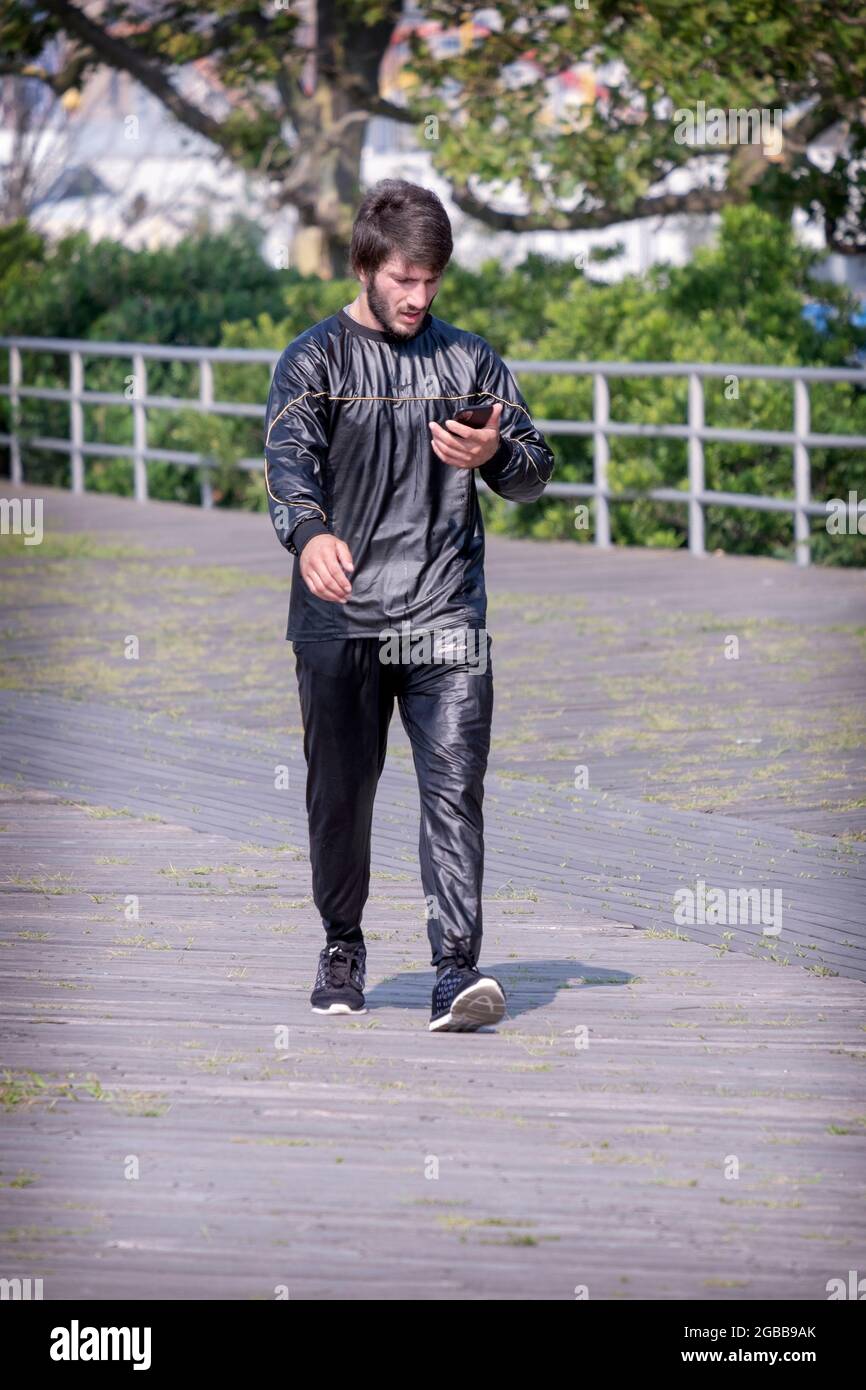 On a very hot NY summer day, a young man exercise walks in a sweat suit and reads his cell phone. In Brighton Beach, Brooklyn, New york City. Stock Photo