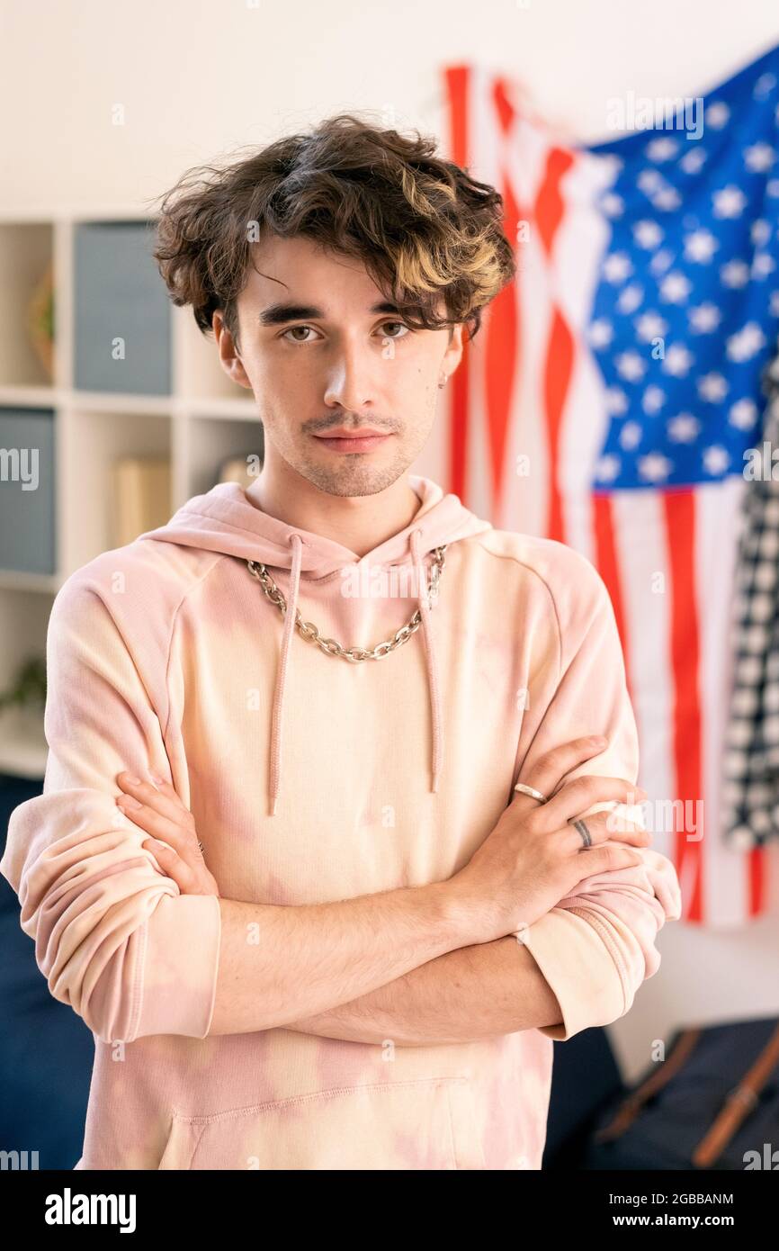 Youthful guy with his arms crossed by chest standing against American flag Stock Photo