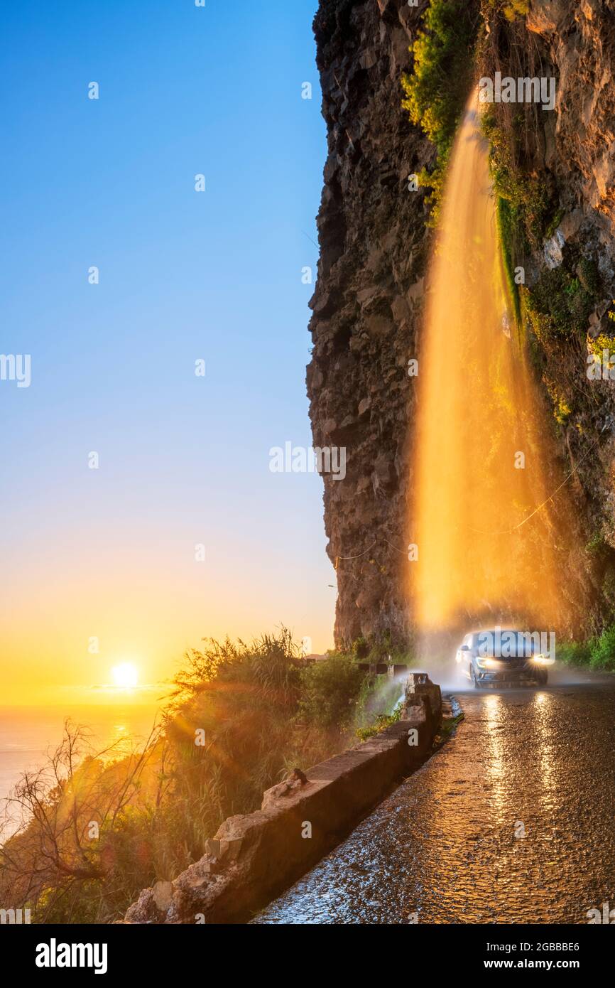 Car passing under Anjos waterfall on slippery coastal road at sunset, Ponta do Sol, Madeira island, Portugal, Atlantic, Europe Stock Photo